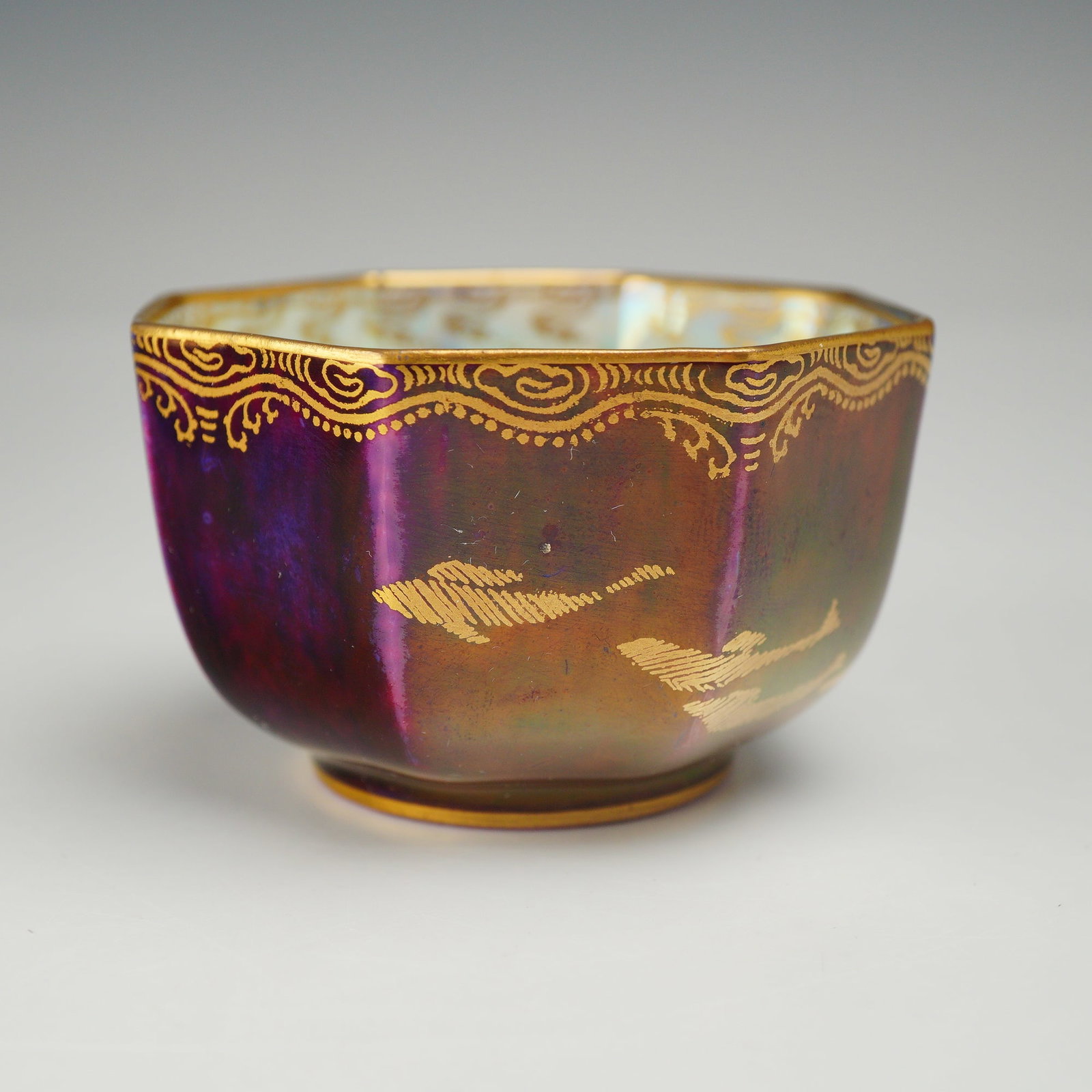 Wedgwood Daisy Makeig-Jones Lustre Octagonal Finger Bowl Pattern Z4827: A Wedgwood bone china octagonal footed bowl designed by Daisy Makeig-Jones. The exterior is decorated with a mottled deep purple and magenta lustre glaze, featuring a gilded scrolling border at the ri