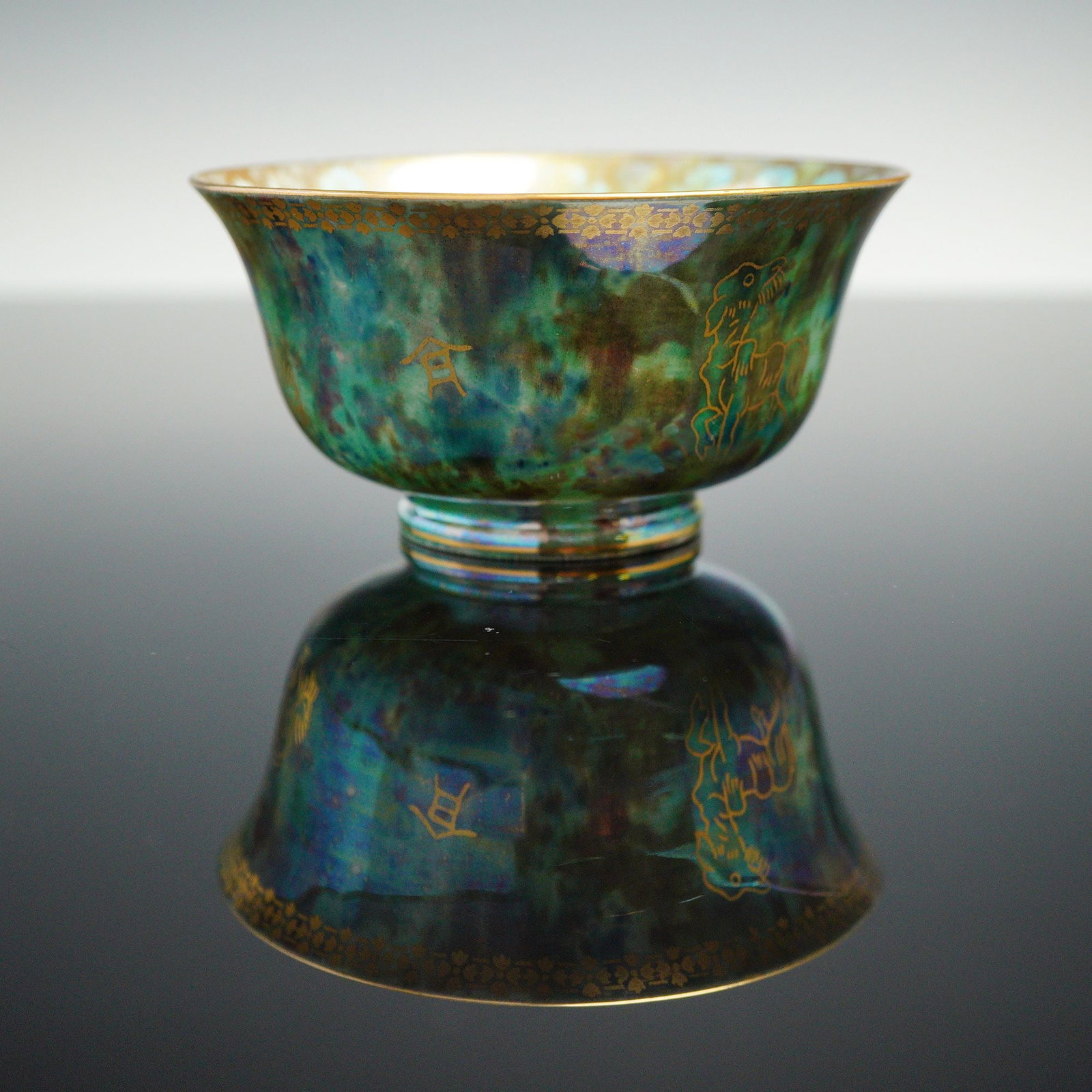 Wedgwood Fairyland Lustre Cup, Coiling Dragon Z4831: Designed by Daisy Makeig-Jones. The footed cup has a mottled green exterior luster glaze with gilt transfer-printed Asian mythical creatures. The rim features a gilded floral border. The interior is f