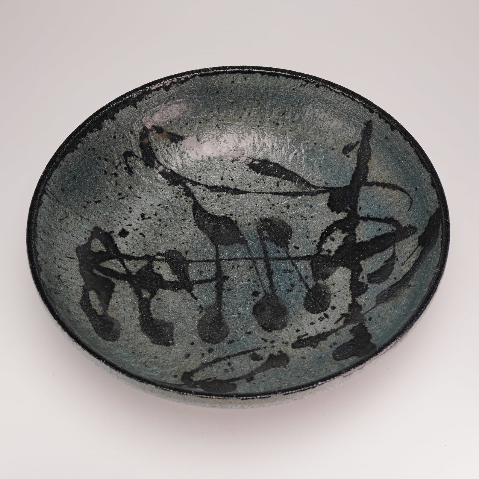 Signed Wedgwood Elwyn James Studio Pottery Bowl: This studio pottery bowl is produced by Wedgwood and signed by artist Elwyn James. The shallow, circular form is made of stoneware featuring a mottled blue and gray-green ground. The interior is decor