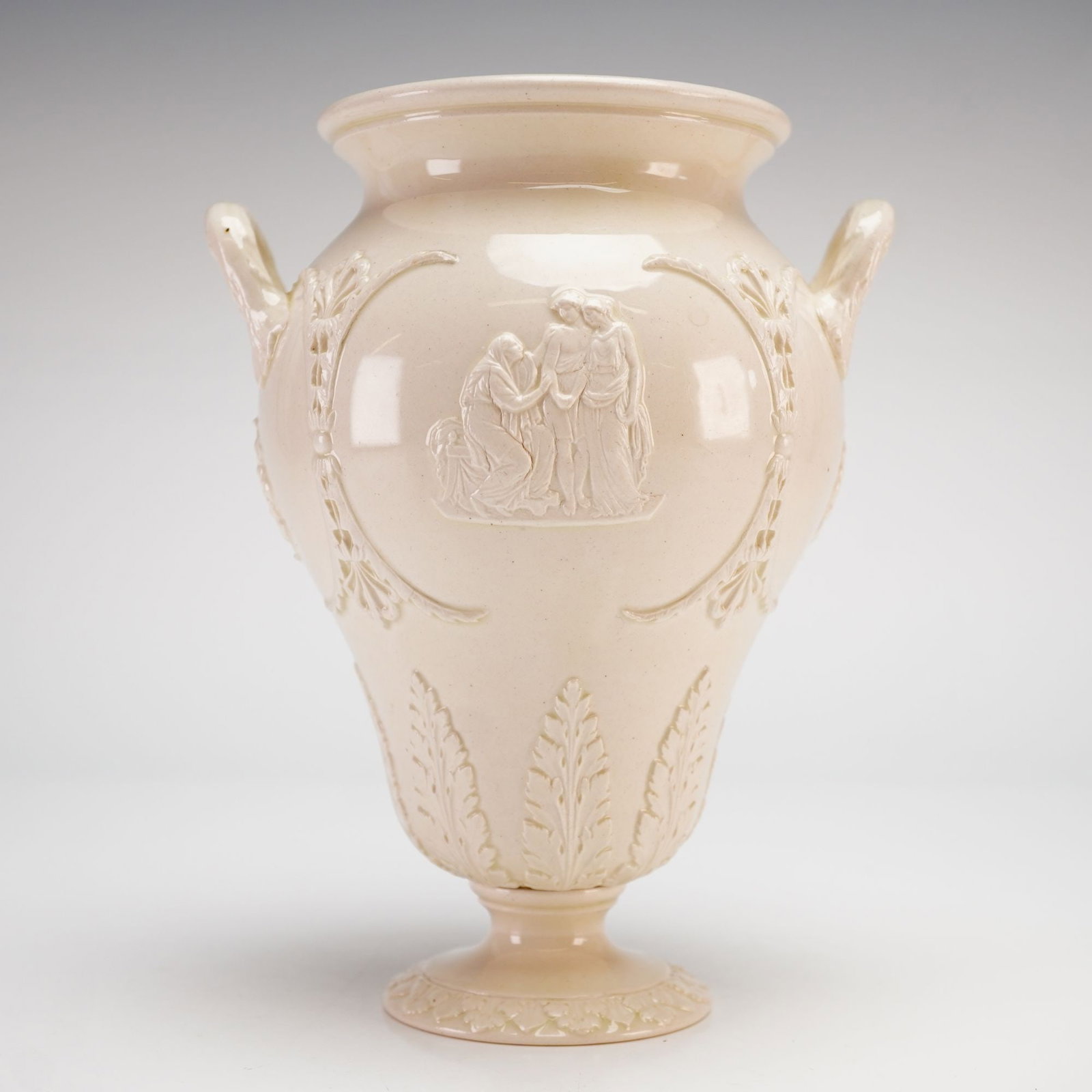 Wedgwood Queensware Double Handled Vase with Neoclassical Figures and Motifs in Raised Relief: This Wedgwood Queensware earthenware vase features a double-handled neoclassical form with a flared rim and a bulbous body supported by a circular footed base. The vessel is finished in a uniform, glo