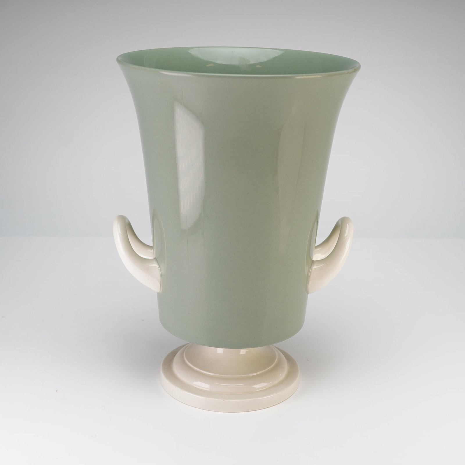 Keith Murray for Wedgwood Etruria & Barlaston Green and White Double Handled Vase: This mid-20th-century ceramic double handled vase was designed by Keith Murray for Wedgwood. The vessel features a flaring cylindrical body finished in a matte celadon green glaze, contrasted by two c