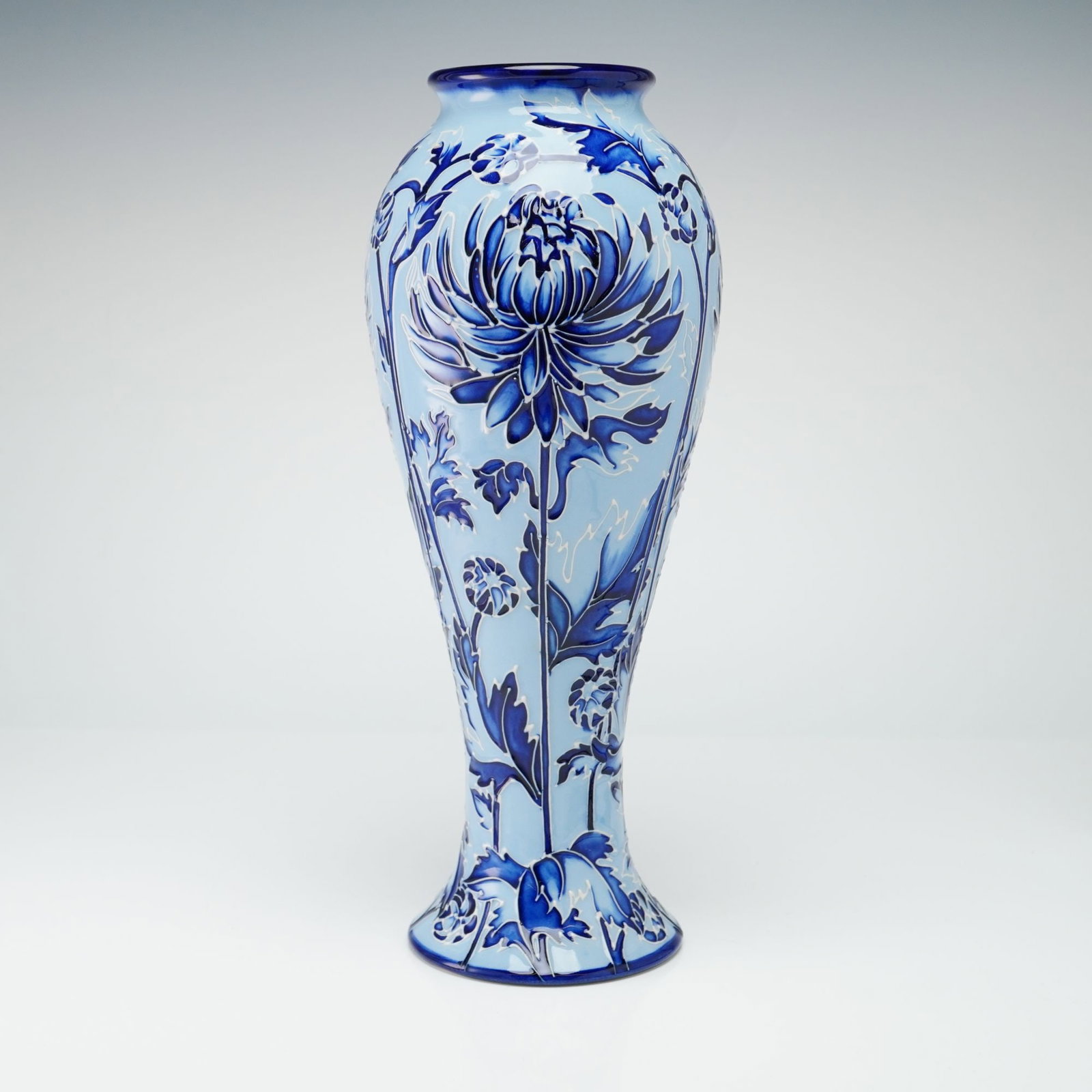 Moorcroft Pottery Modern Florian Ware Blue Chrysanthemum Vase: The exterior is hand-decorated using the signature tube-lining technique, which creates raised slip outlines for the stylized chrysanthemum blooms and trailing foliage. The decorative scheme utilizes 