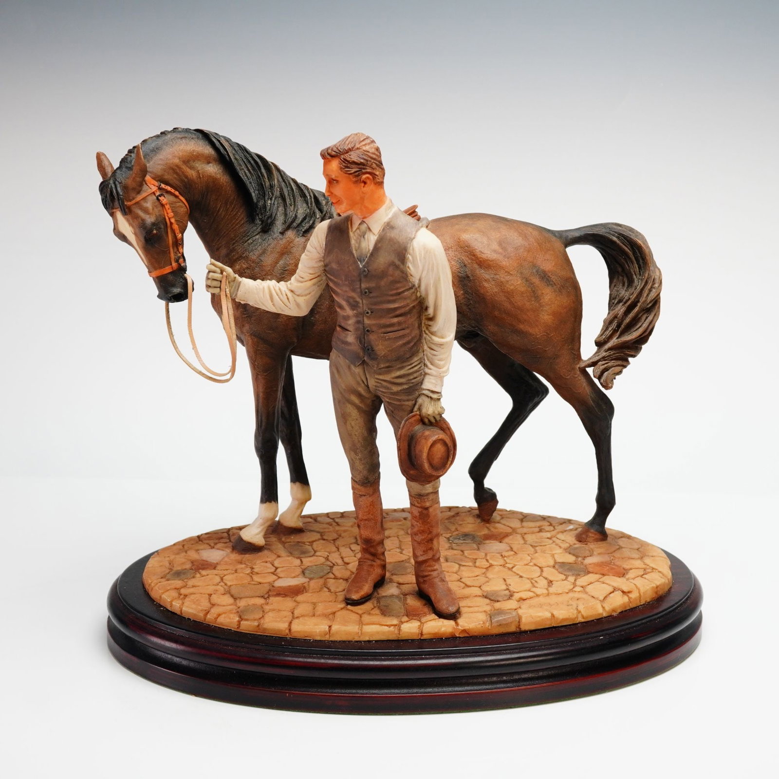 Jose Luis Cassola Polychrome Resin Equestrian Sculpture of a Man and Horse: A hand-painted polychrome resin sculpture by Jose Luis Cassola, depicting a man in equestrian attire standing beside a saddled bay horse. The figure is rendered with realistic detail, wearing a waistc