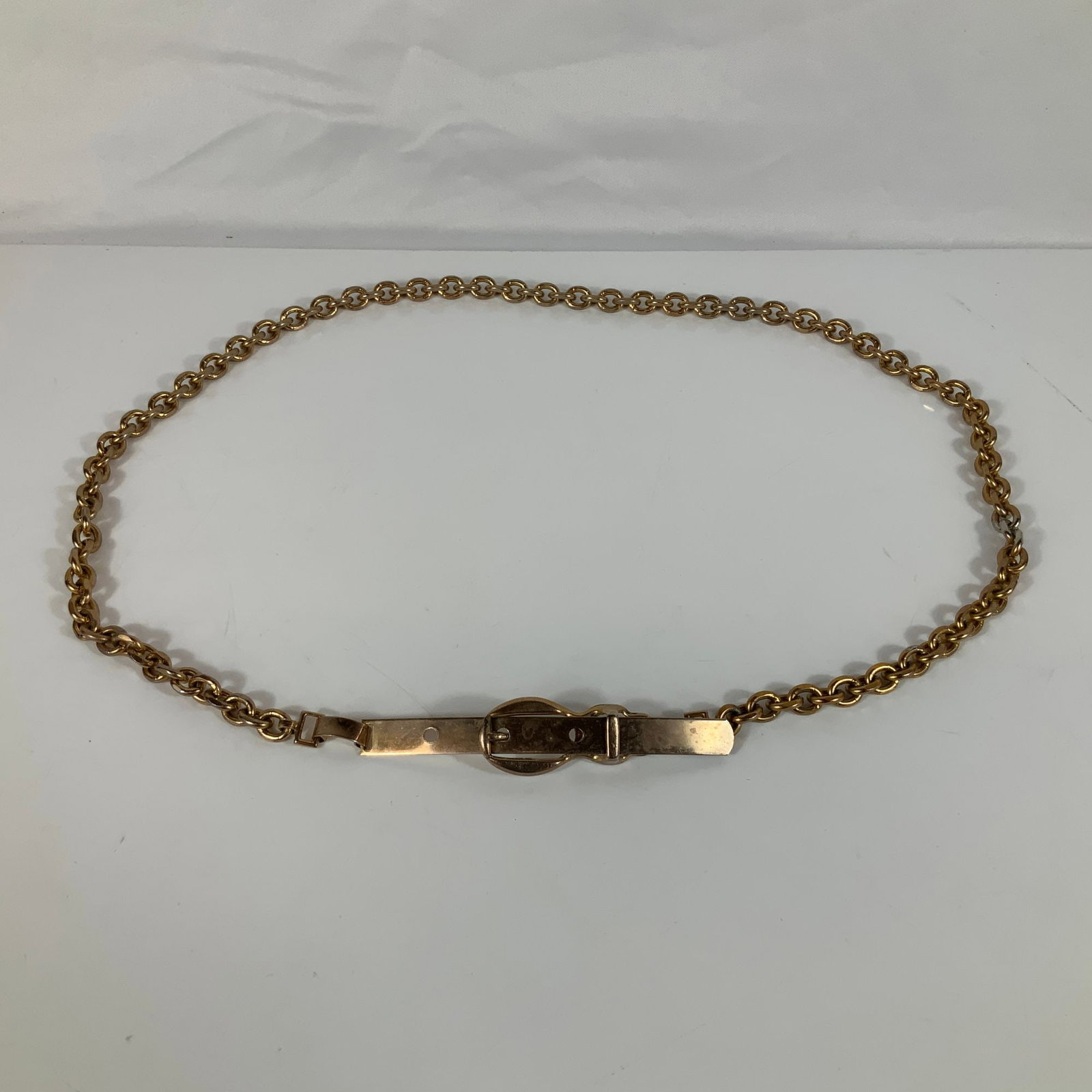 Gold-Toned Heavy Link Chain Belt: This fashion accessory is a gold-toned metal chain belt featuring a heavy circular-link construction. The piece is designed with a unique closure system that includes a flat, rectangular metal strap w