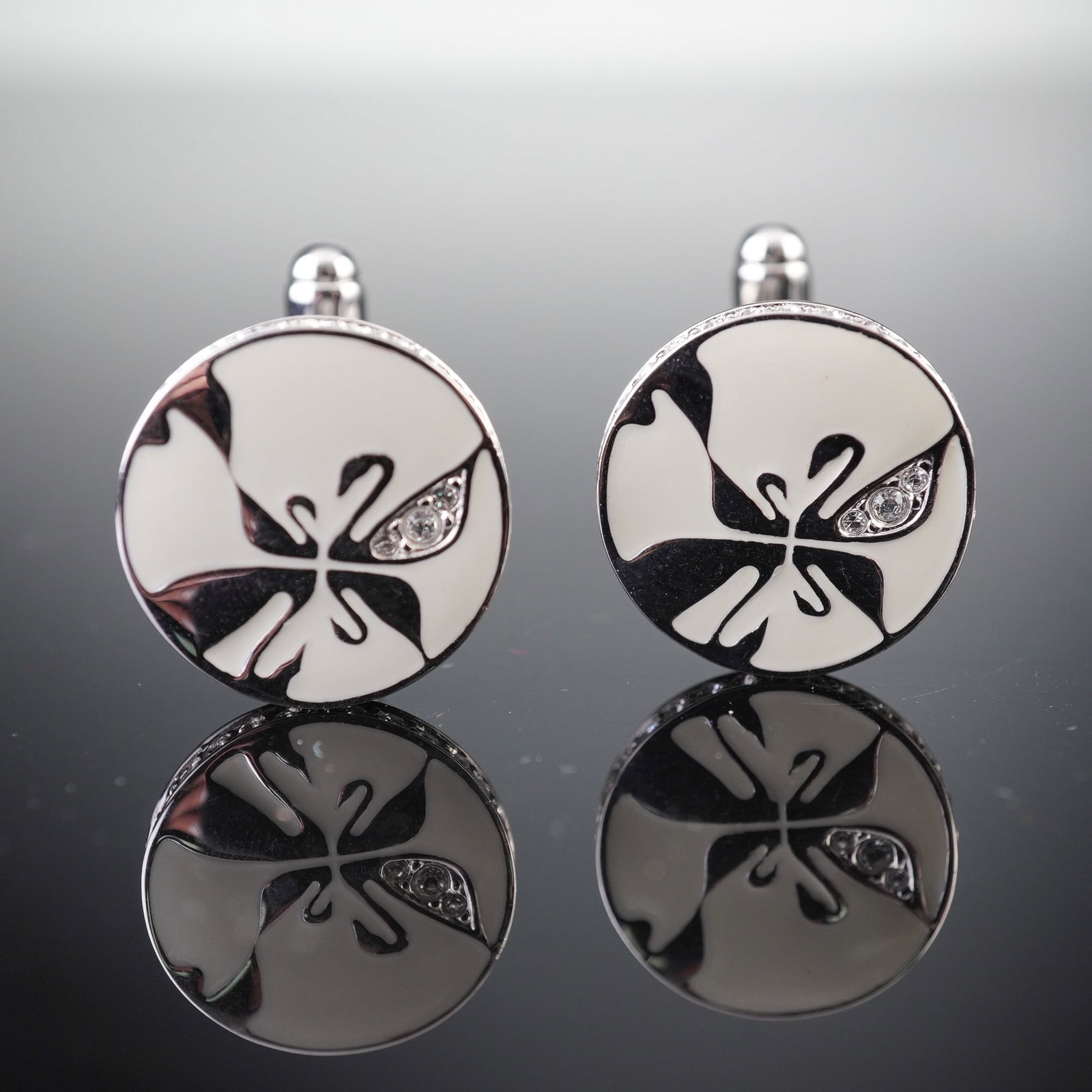A Pair of Swarovski Silver-Tone and Enamel Black Swan Motif Cufflinks: A pair of Swarovski silver-tone cufflinks, each featuring a round face with a white enamel or resin inlay depicting a stylized black swan motif, accented by small clear stones. Further clear stones ar