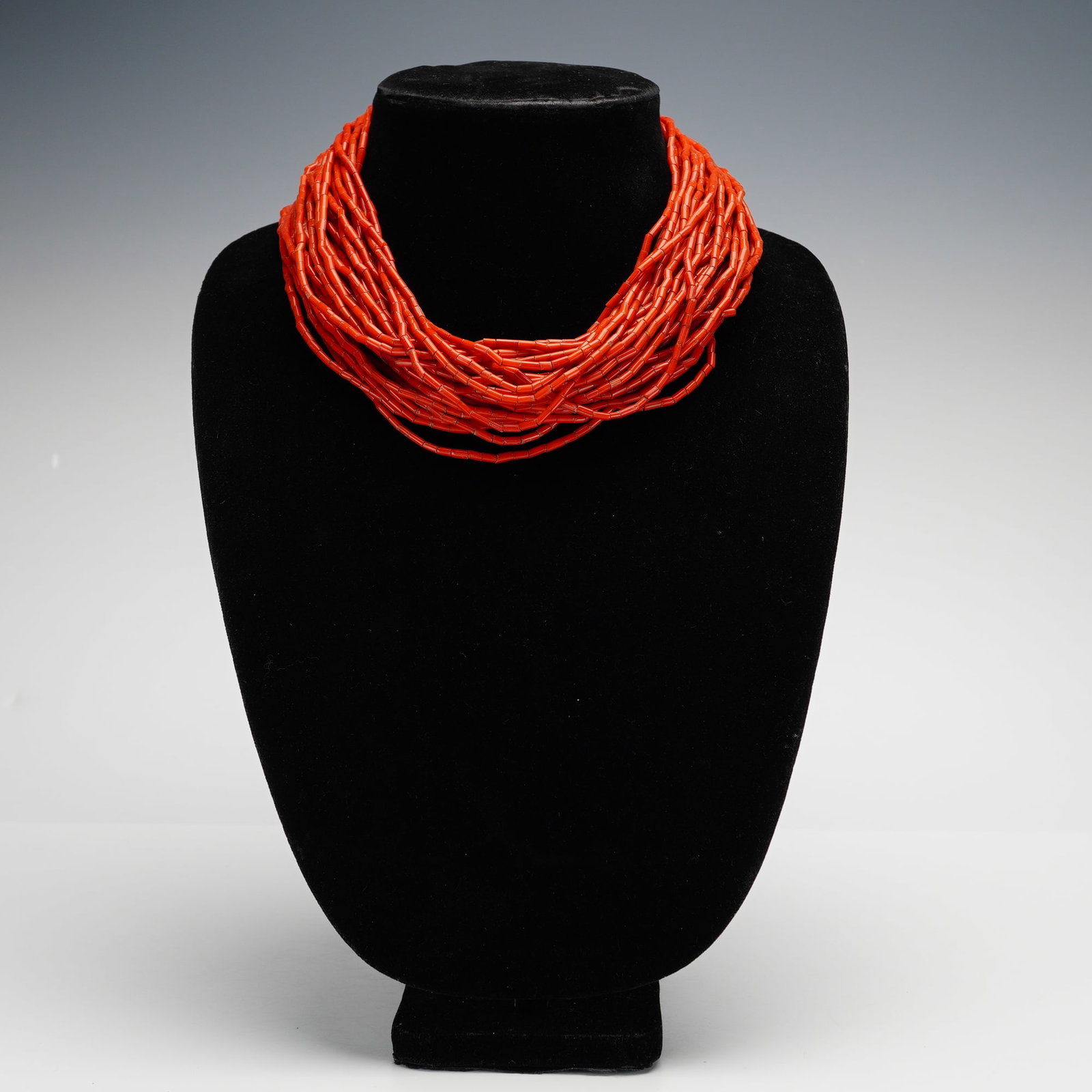 Konyak Naga Style Multi Strand Red Glass Bead Necklace: This multi-strand red glass bead necklace is composed of numerous rows of vibrant orange-red tubular beads. The strands are accented with small blue, yellow, and turquoise-colored seed beads where the