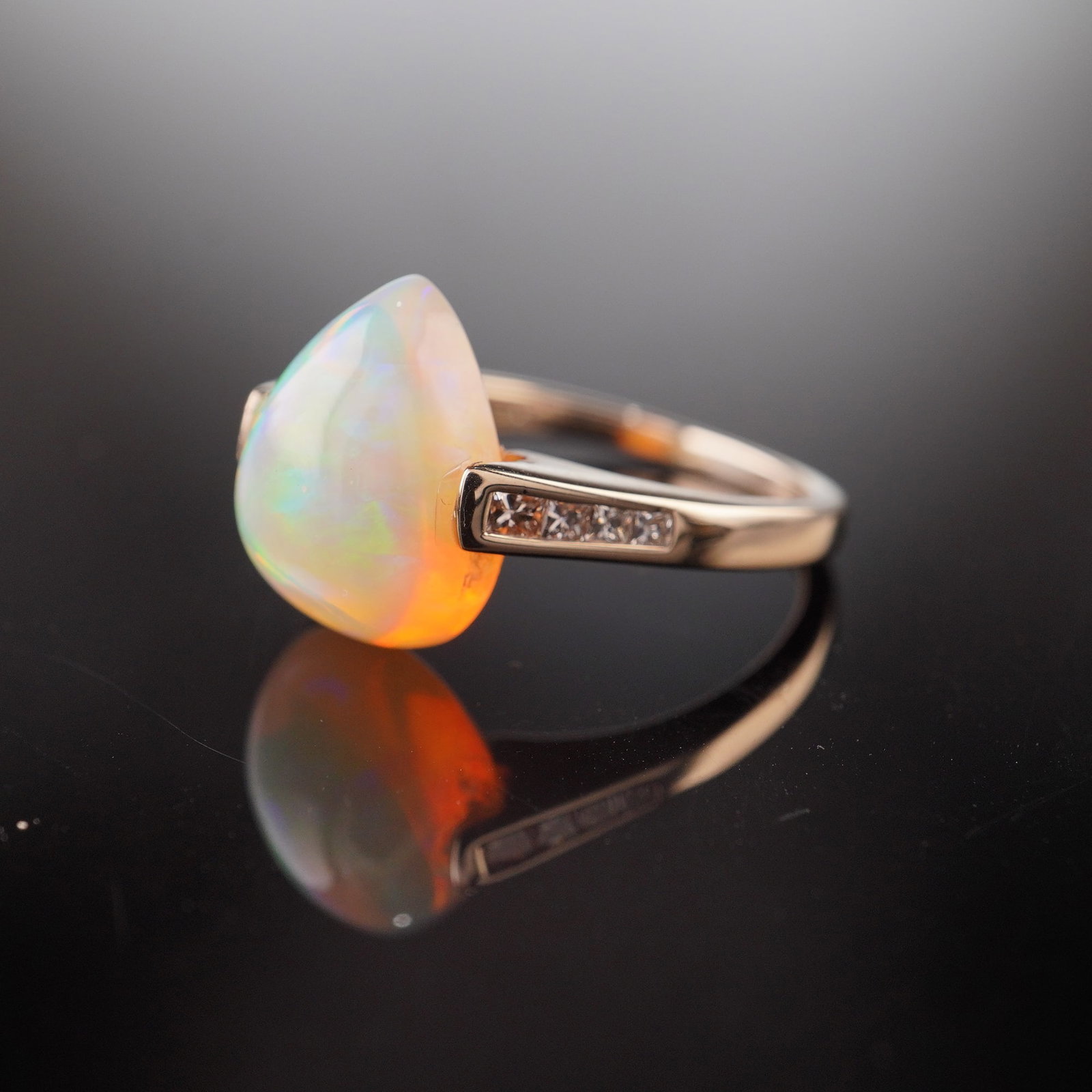 14K Gold 4.12ct Opal and Diamond Ring: A yellow gold ring featuring a pear-shaped opal, shouldered by four princess-cut diamonds on each side, totaling eight diamonds. The band is marked 14K and IKS. Dimensions: Ring size: 6.25 Weight: 3.1