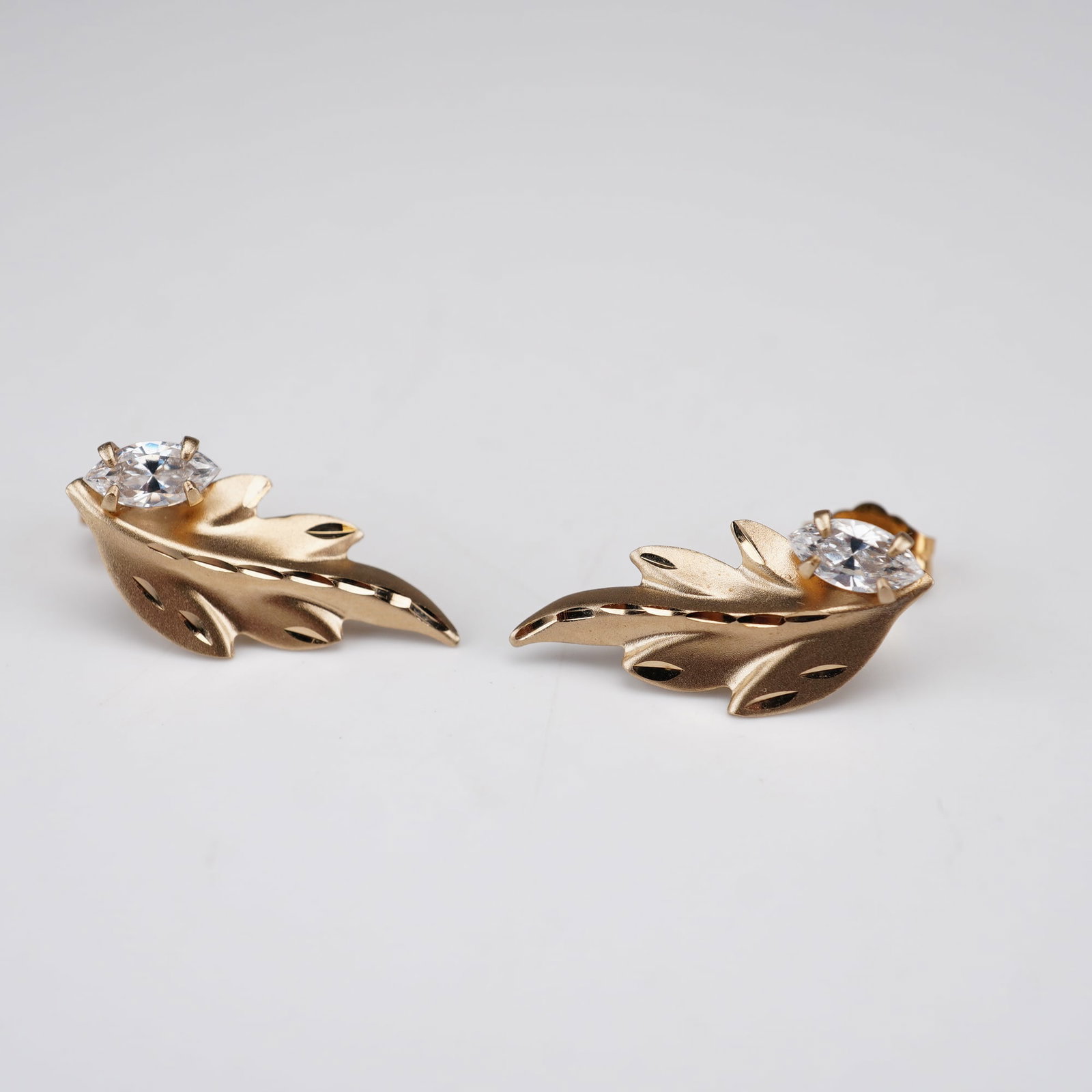A Pair of Princess Pride Creations 14K Gold and Cut Stone Leaf Stud Earrings: A matched pair of textured leaf-form stud earrings. Each earring features a realistically rendered leaf with a satin and matte finish accented by bright-cut engraving along the veins and edges. A sing