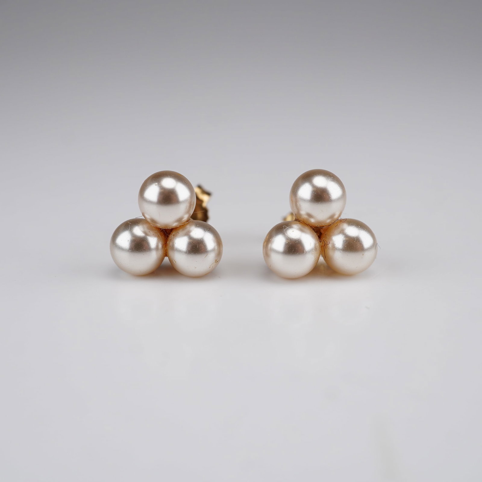 A Pair of Majorca Pearl Cluster Stud Earrings with 14K Gold Posts: A matched pair of stud earrings featuring a trefoil cluster of three round, cream-colored Majorca pearls. Majorca pearls are a recognized brand of high-quality imitation pearls known for their luster 