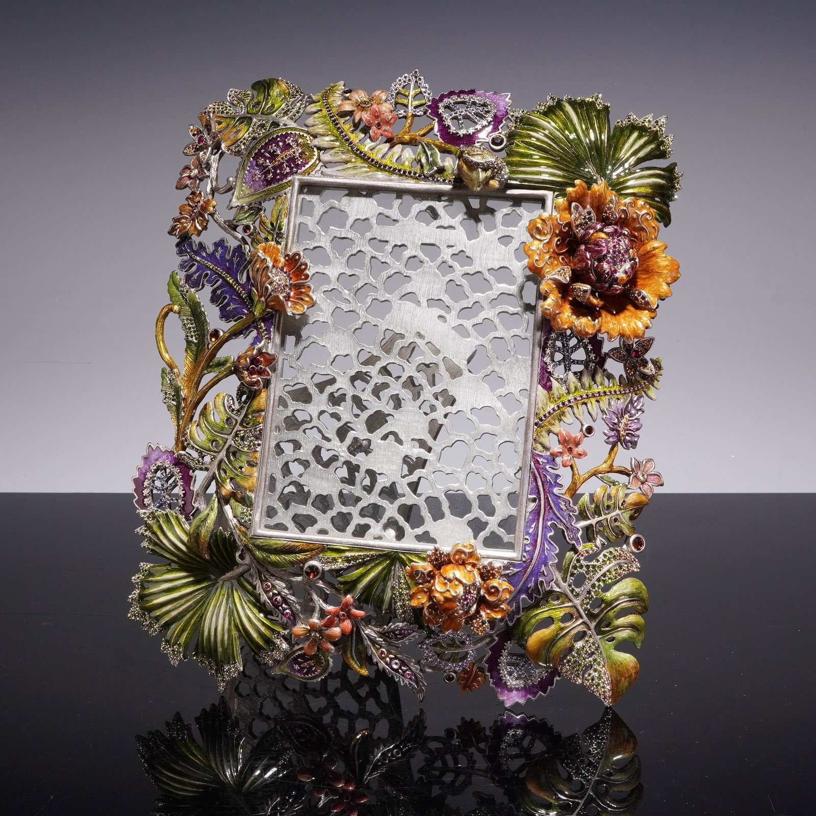 Jay Strongwater Cluster Floral Bouquet Picture Frame: A contemporary Jay Strongwater tabletop picture frame constructed of cast metal with an elaborate botanical design featuring a dense arrangement of exotic foliage and flora, including monstera leaves,