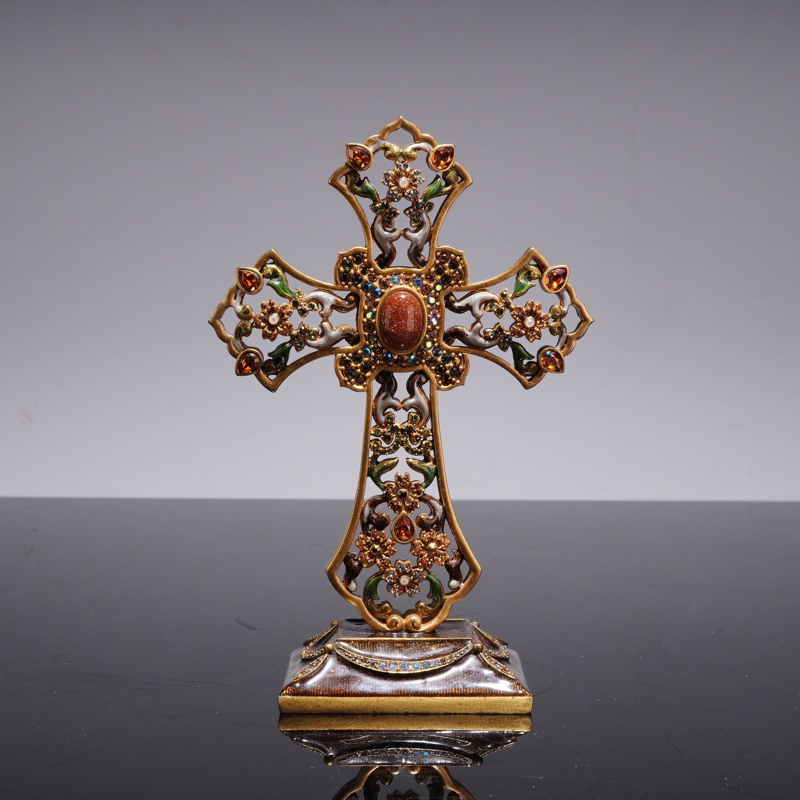 Jay Strongwater Jeweled Standing Cross: A Jay Strongwater jeweled standing cross constructed from cast metal with a gold-tone finish, featuring hand-applied enamel and hand-set crystals. The cross displays an intricate openwork design of sc