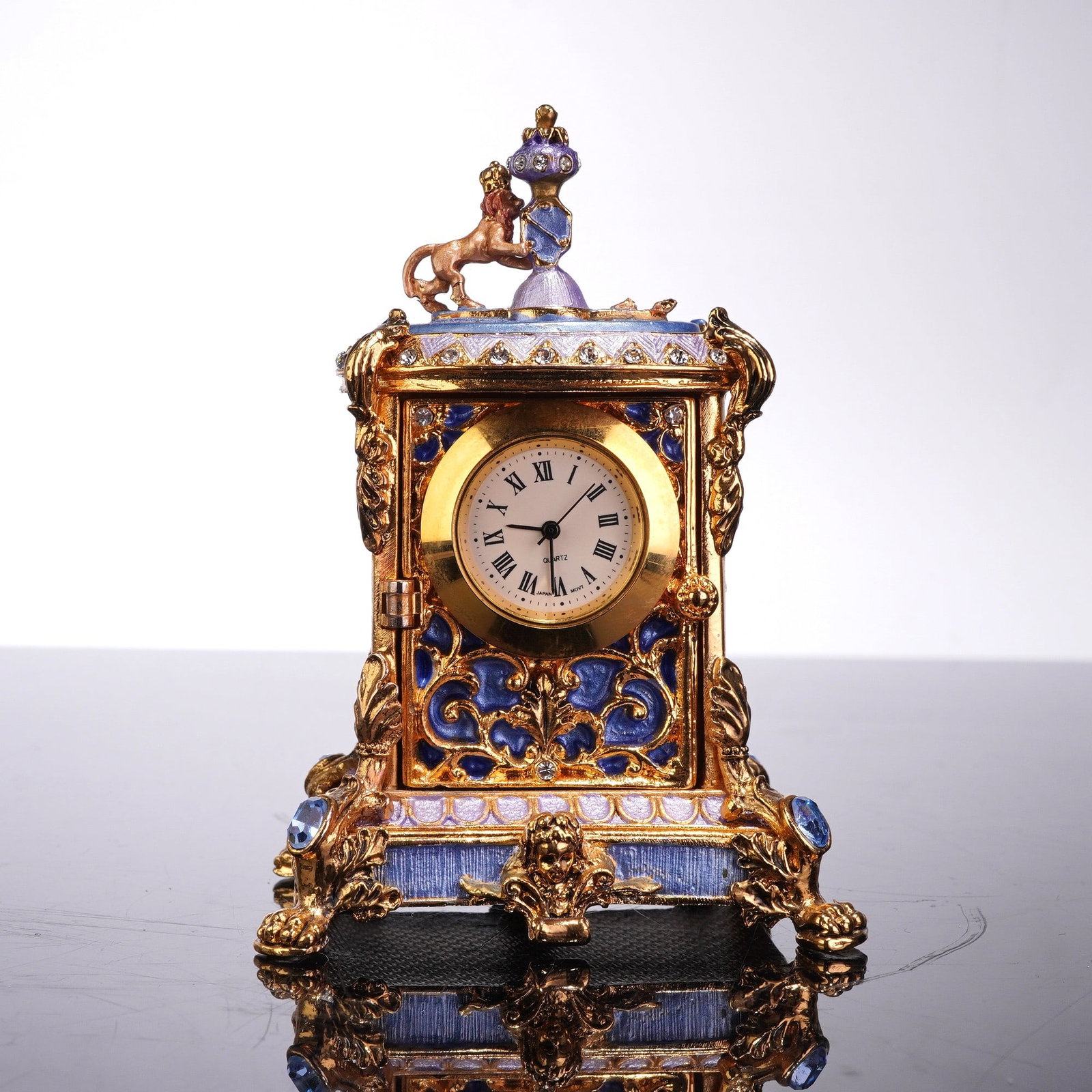 Style of Jay Strongwater Enameled Metal Miniature Mantle Clock: This miniature mantle clock in the style of Jay Strongwater, featuring a maker's circular mark on the underside. The item is constructed from gold-tone enameled metal and functions as both a timepiece