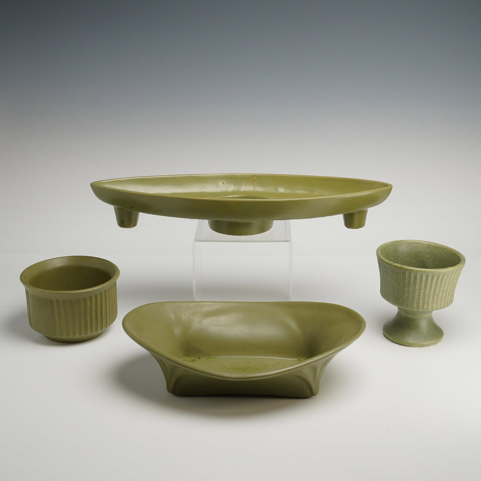 A Collection of Floraline and McCoy Green Pottery Bowls and Candleholders: A collection of mid-century modern ceramic floral vessels and containers from the Floraline line by McCoy, finished in a uniform matte olive green glaze. The group includes an elongated almond-shaped 