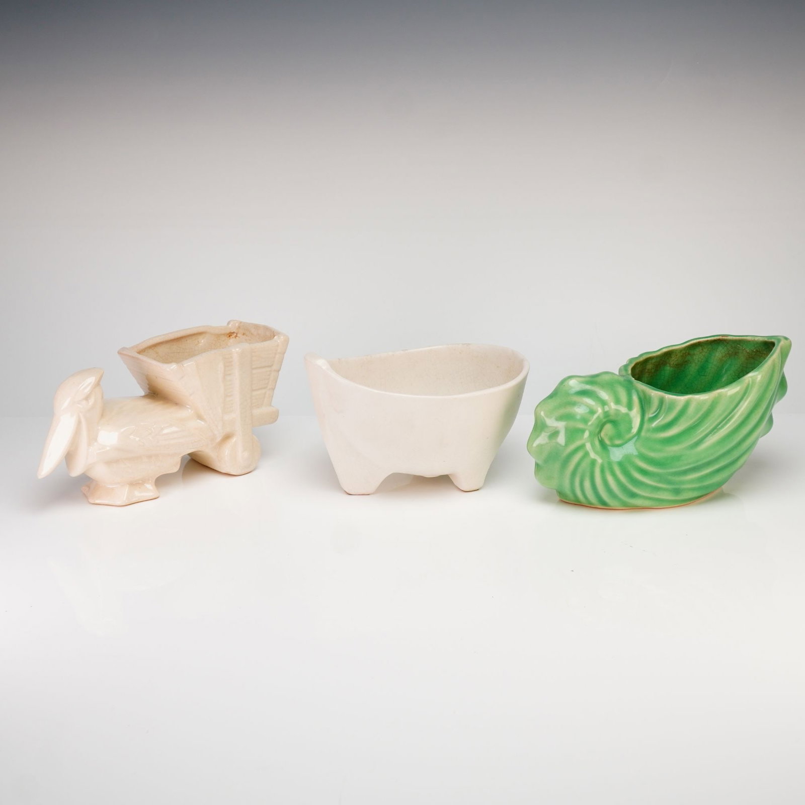 Three McCoy Pottery Glazed Ceramic Planters and Green Shell Planter: A collection of three vintage McCoy Pottery glazed ceramic planters featuring distinct mid-century forms. The group includes a green nautilus shell-shaped vessel with a ribbed texture, a cream-colored