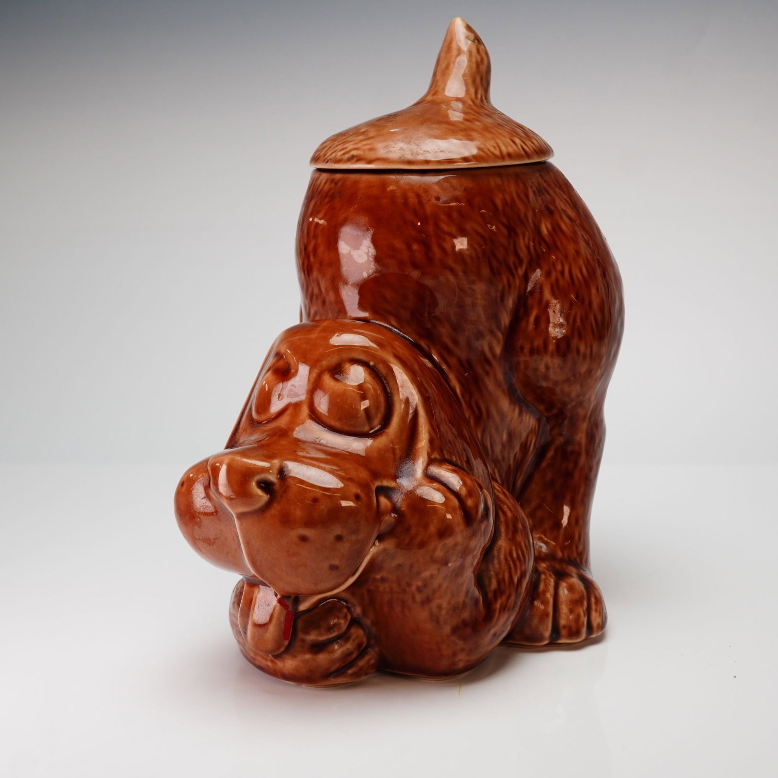 McCoy 0272 Brown Thinking Hound Dog Ceramic Cookie Jar: This McCoy Thinking Hound Dog cookie jar, model 0272, is constructed of glazed ceramic. The form depicts a stylized hound in a crouching position with its tongue extended. The exterior is finished in 