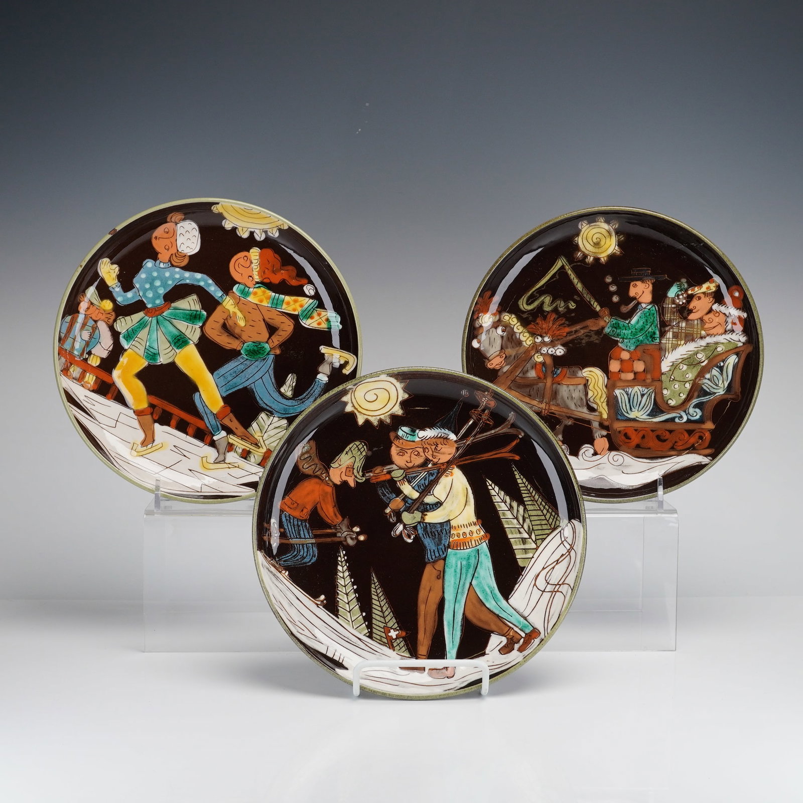 Arnold Zahner Rheinfelden Winter Folk Art Decorative Wall Plates: This set of three Arnold Zahner Rheinfelden decorative wall plates features whimsical winter scenes in a mid-century folk-art style. Produced by the Zahner pottery studio in Rheinfelden, Switzerland,
