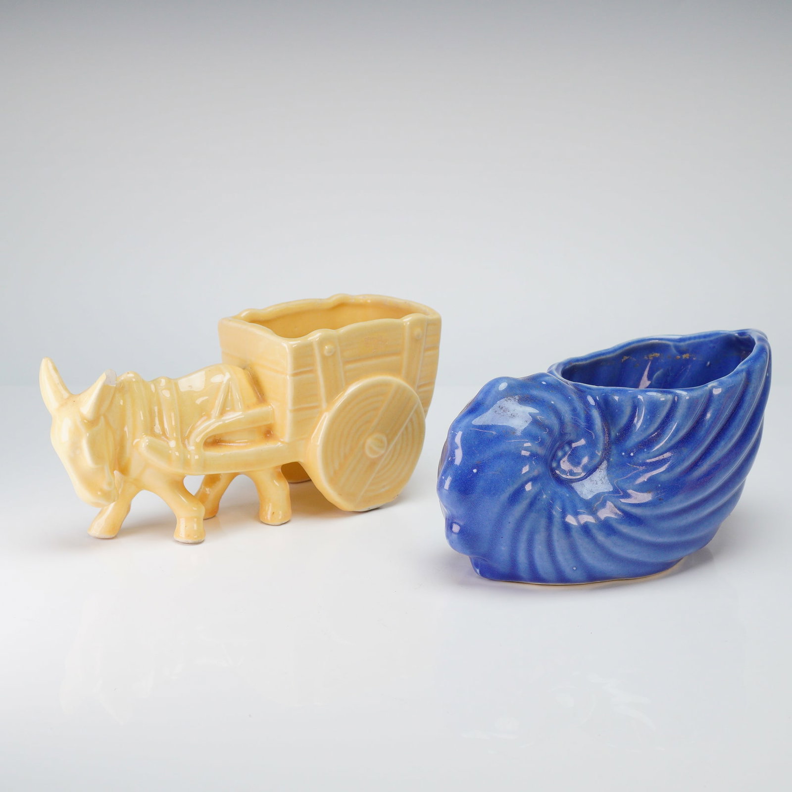American Art Pottery, Donkey Cart and Nautilus Shell Planters: This lot features two vintage American art pottery planters from the mid-20th century. The first is a stylized donkey pulling a two-wheeled cart with a wood-grain texture, finished in a uniform pale y