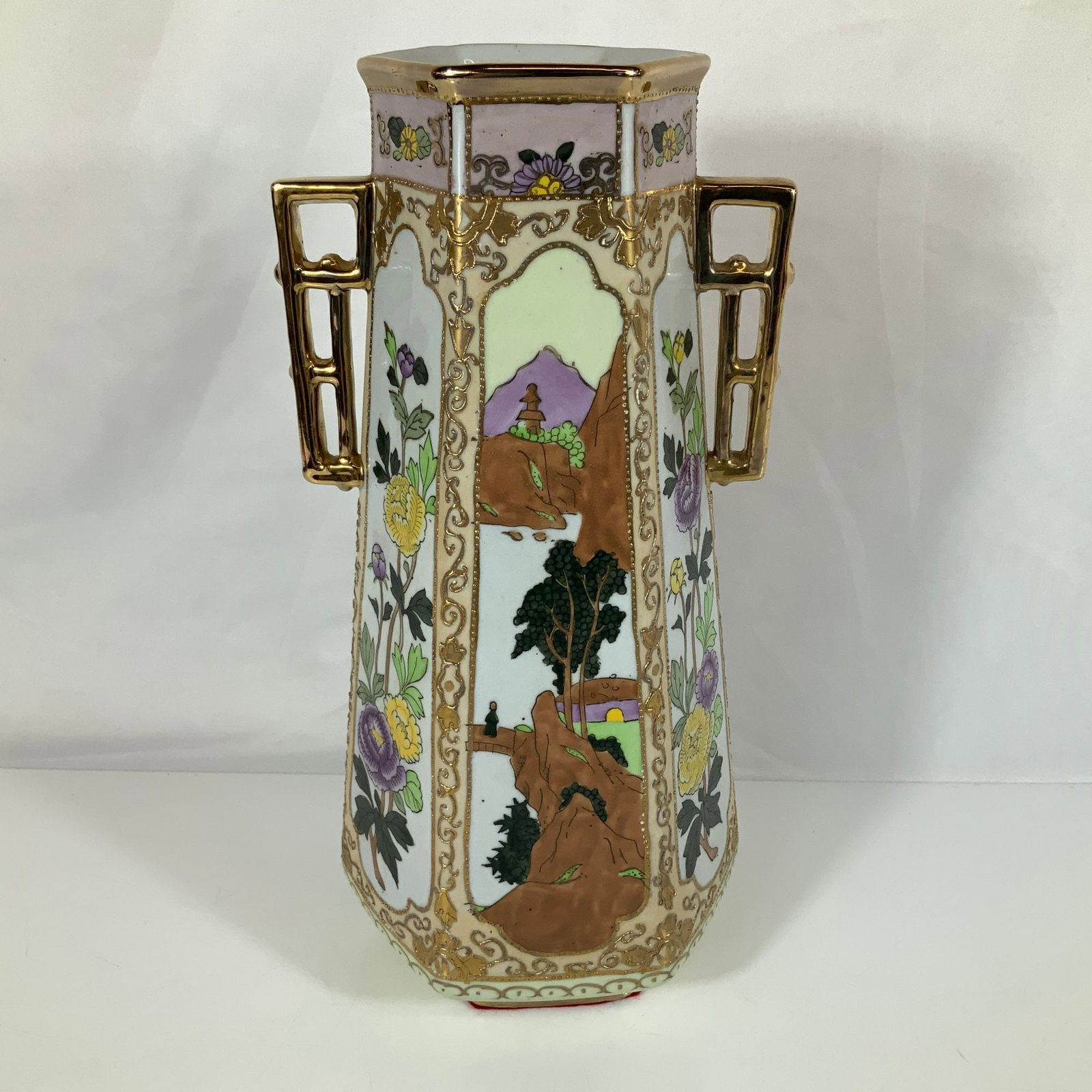 Nippon Hand Painted Scenic and Floral Hexagonal Porcelain Vase Signed Marilyn Fels 1978: A hand painted porcelain vase featuring a tapering hexagonal body and two openwork geometric handles at the shoulder finished in a bright gold glaze. The form and style are consistent with Nippon porc