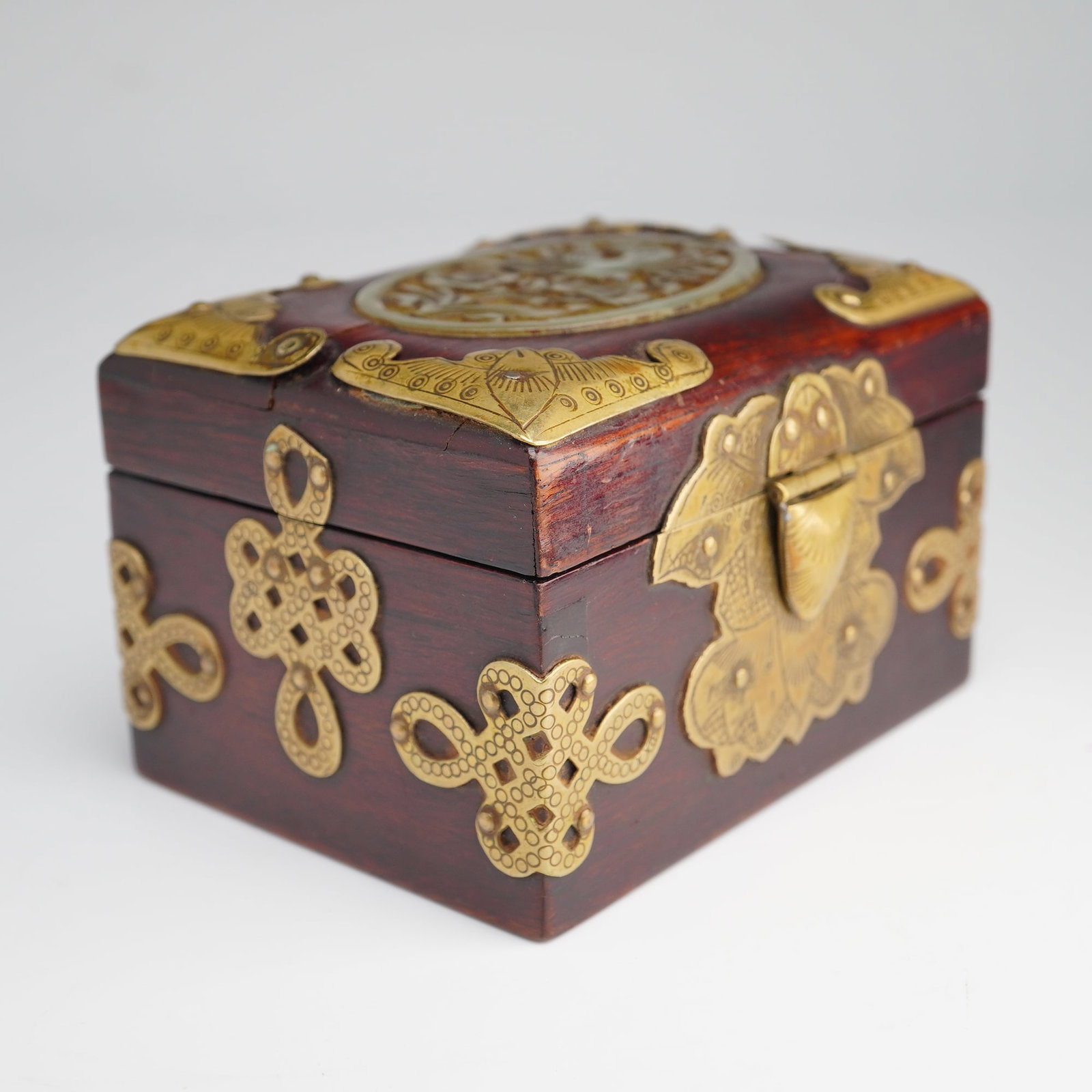 Early 20th Century Chinese Hongmu and Brass-Mounted Jewelry Box with Carved Jade Plaque: An early 20th century Chinese wooden box with brass accents and stone decorative feature on top, meticulously crafted from polished hongmu rosewood. The piece is heavily ornamented with hand-chased br