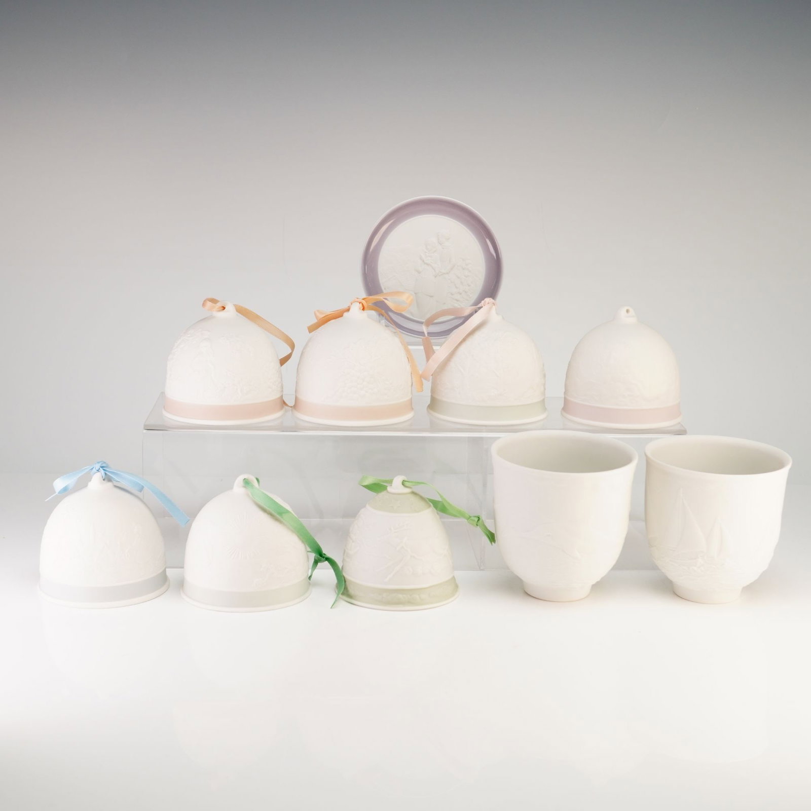 Collection of Ten Lladro Collectors Society Bisque Porcelain- Bells, Cups and Dish: This collection includes ten items produced by Lladro for the Collectors Society, featuring matte bisque porcelain with detailed bas-relief decoration. The set is comprised of seven holiday bell ornam