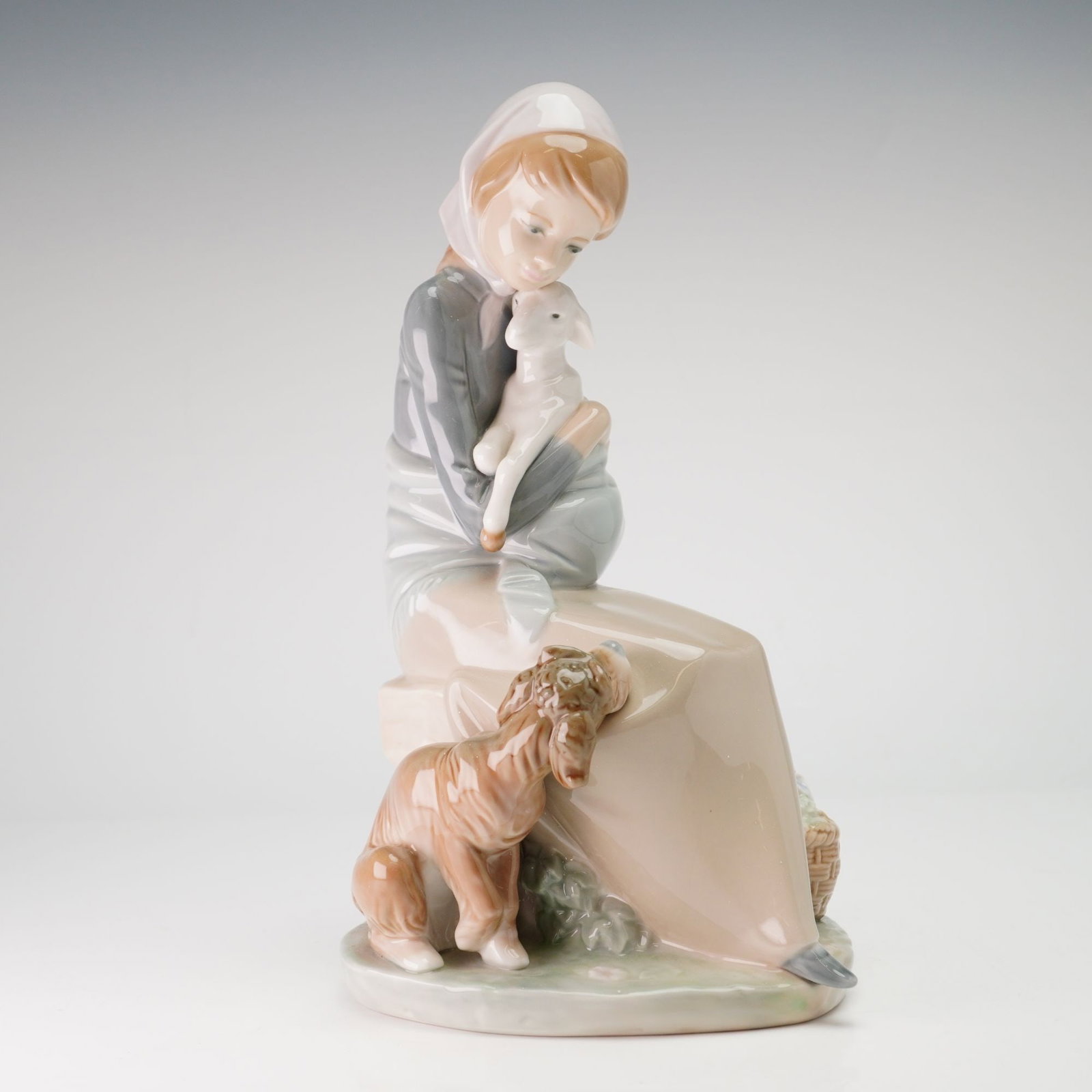 Lladro Porcelain Figurine, Jealousy/Devotion 01001278: Lladro glazed porcelain figurine titled Jealousy was designed by sculptor Juan Huerta. The figurine depicts a young girl seated on a rock, dressed in a grey long-sleeved tunic, a long tan skirt, and a