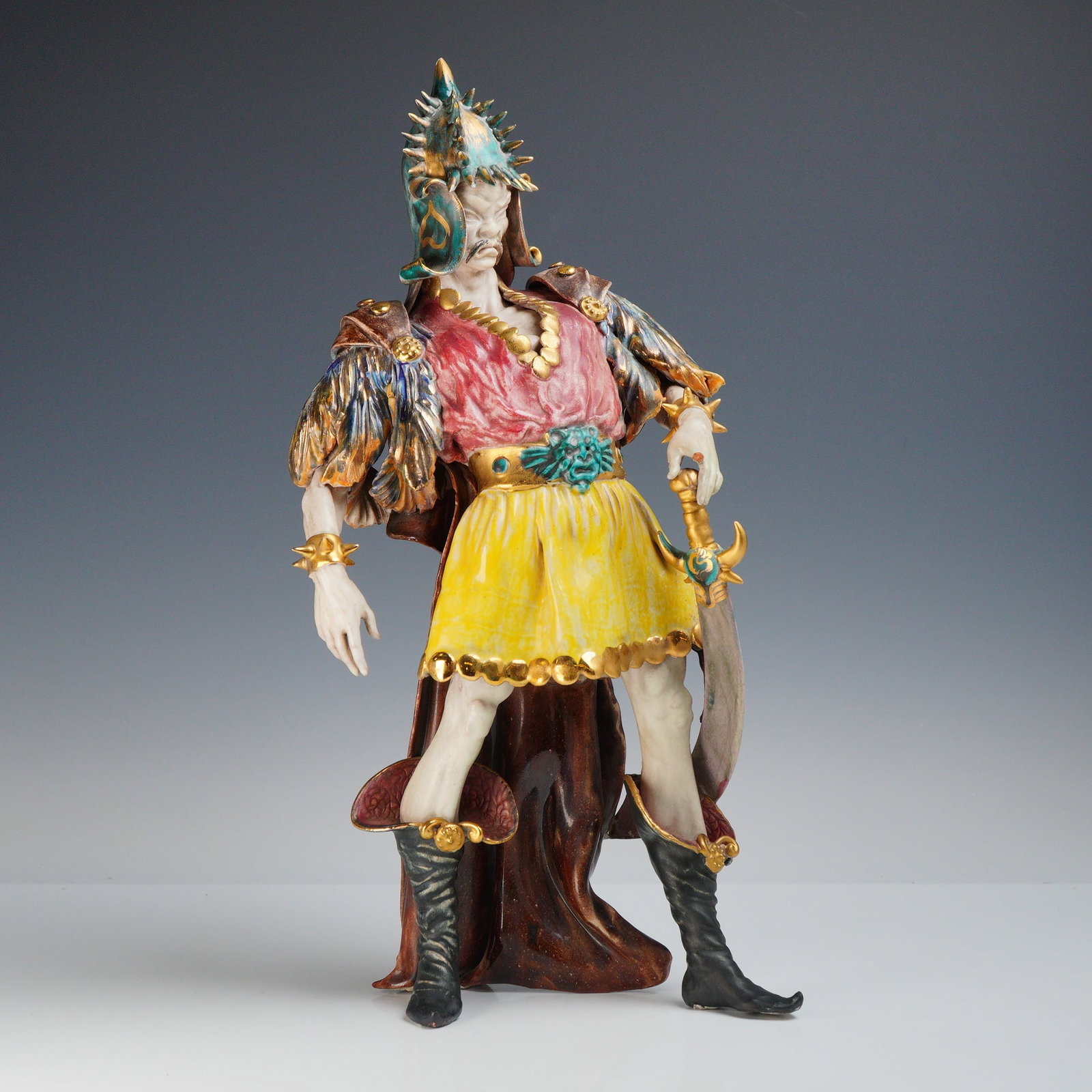 Gino Danti Mongolian Warrior Italian Art Pottery Figurine: This ceramic figurine is identified as a Mongolian warrior by the Italian artist Gino Danti. The figure is depicted in a theatrical pose, wearing an ornate costume consisting of a spiked helmet with t