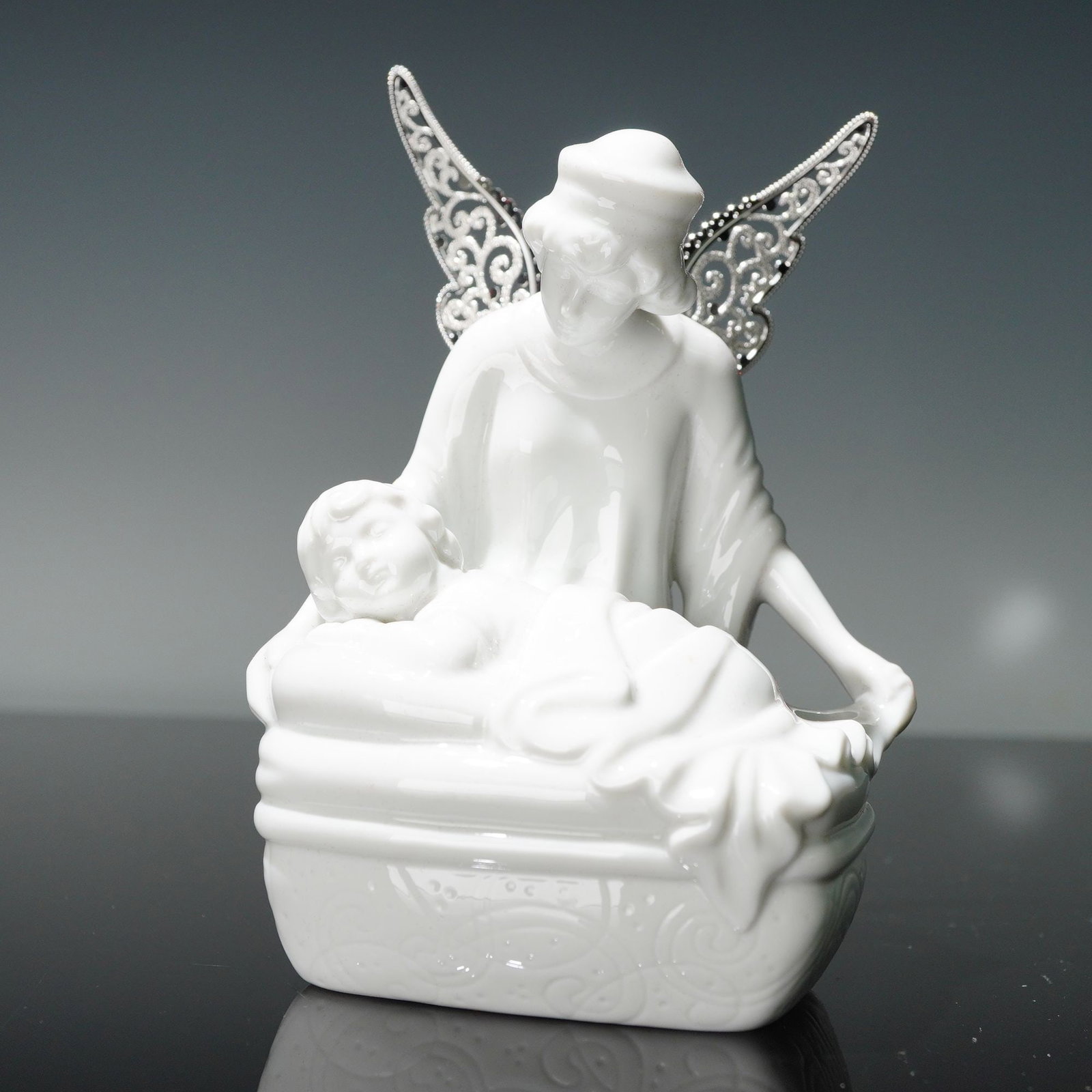 Newbridge Silverware Porcelain Mother and Child Figurine: Porcelain figurine depicting a mother and child, designed with intricate silver-tone filigree wings attached at the back. Features an embossed decorative base with an overall glossy white glaze highli