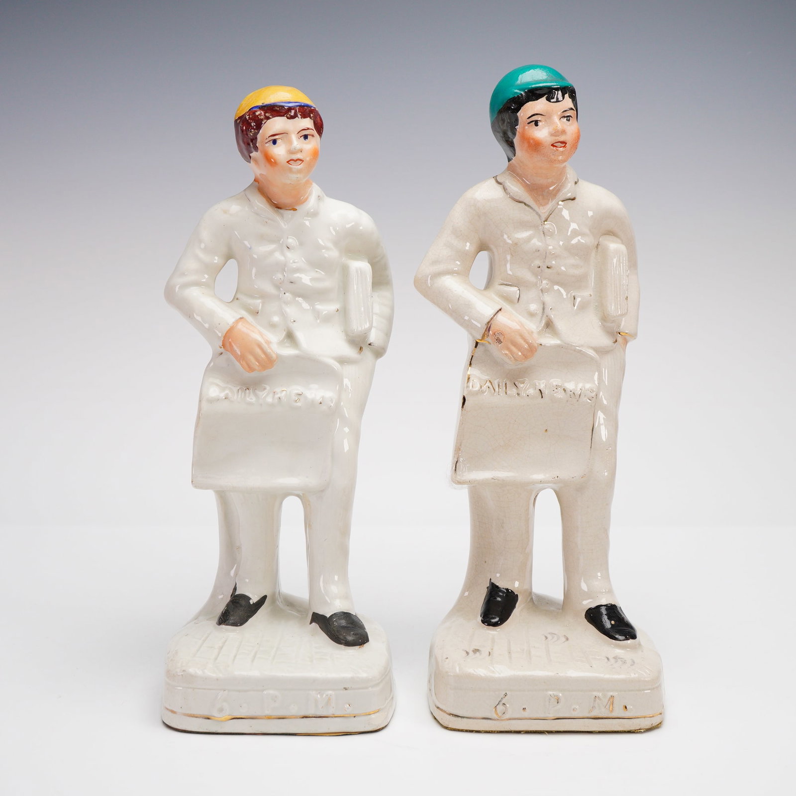 2pc Antique Staffordshire Sculptures , Daily News 6PM: Victorian-era Staffordshire porcelain figurines depicting young newspaper delivery boys, each holding a "Daily News" bag marked 6 P.M. at the base. These figures, commonly attributed to Staffordshire 