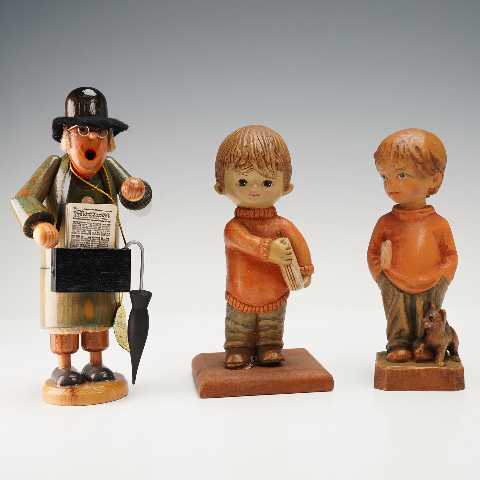 3pc Wooden Newspaper Themed Figurines: Grouping of three carved and painted wooden figures, each depicted holding newspapers. Includes one Handarbeit Erzgebirgische Volkskunst figure of a man with paper and umbrella, another marked E. Schm