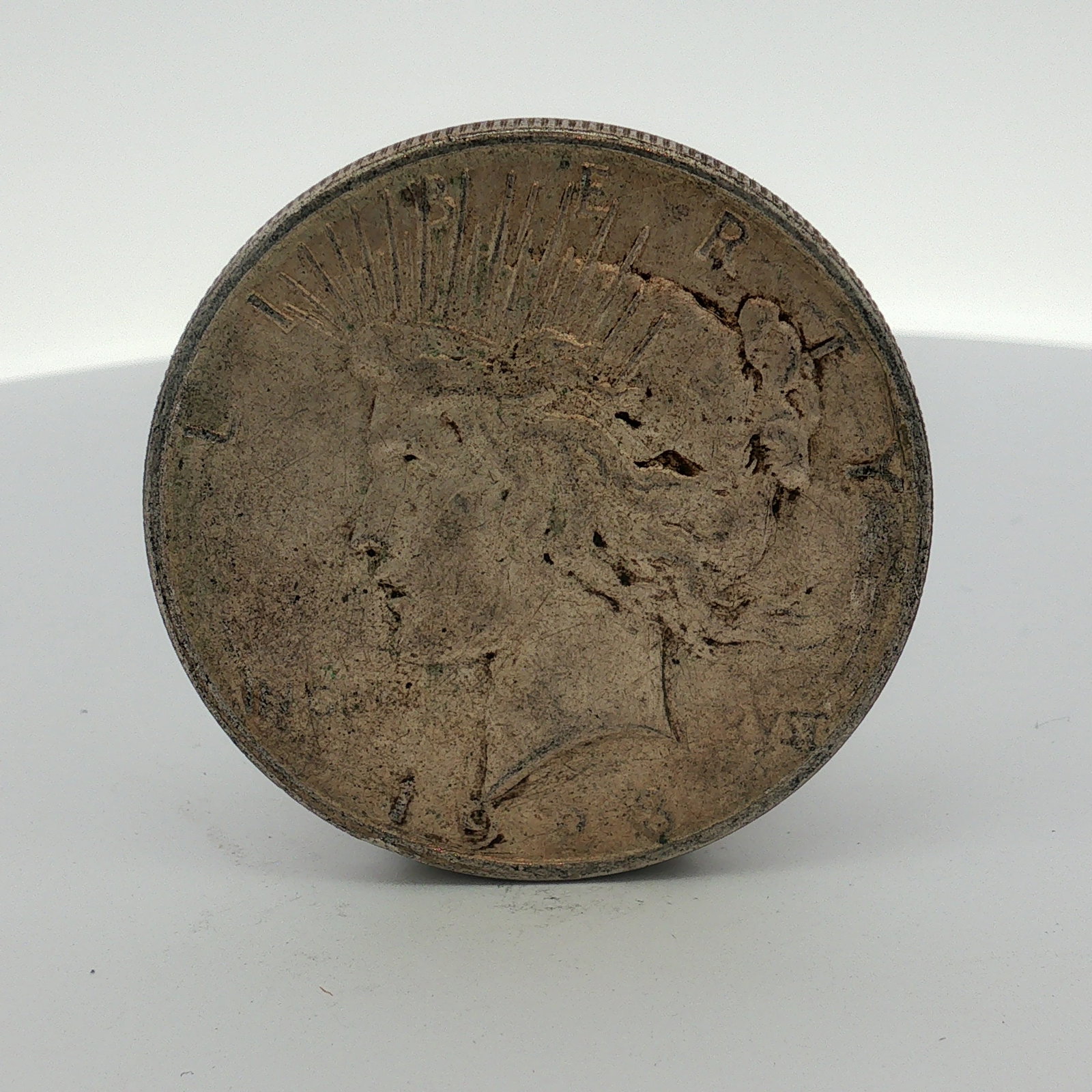 1923-D US One Dollar Peace Silver Dollar, Circulated: This US Peace silver dollar is a struck 90% silver coin featuring a Liberty head obverse and an eagle reverse. The obverse displays the legend LIBERTY and the partially obscured motto IN GOD WE TRVST,