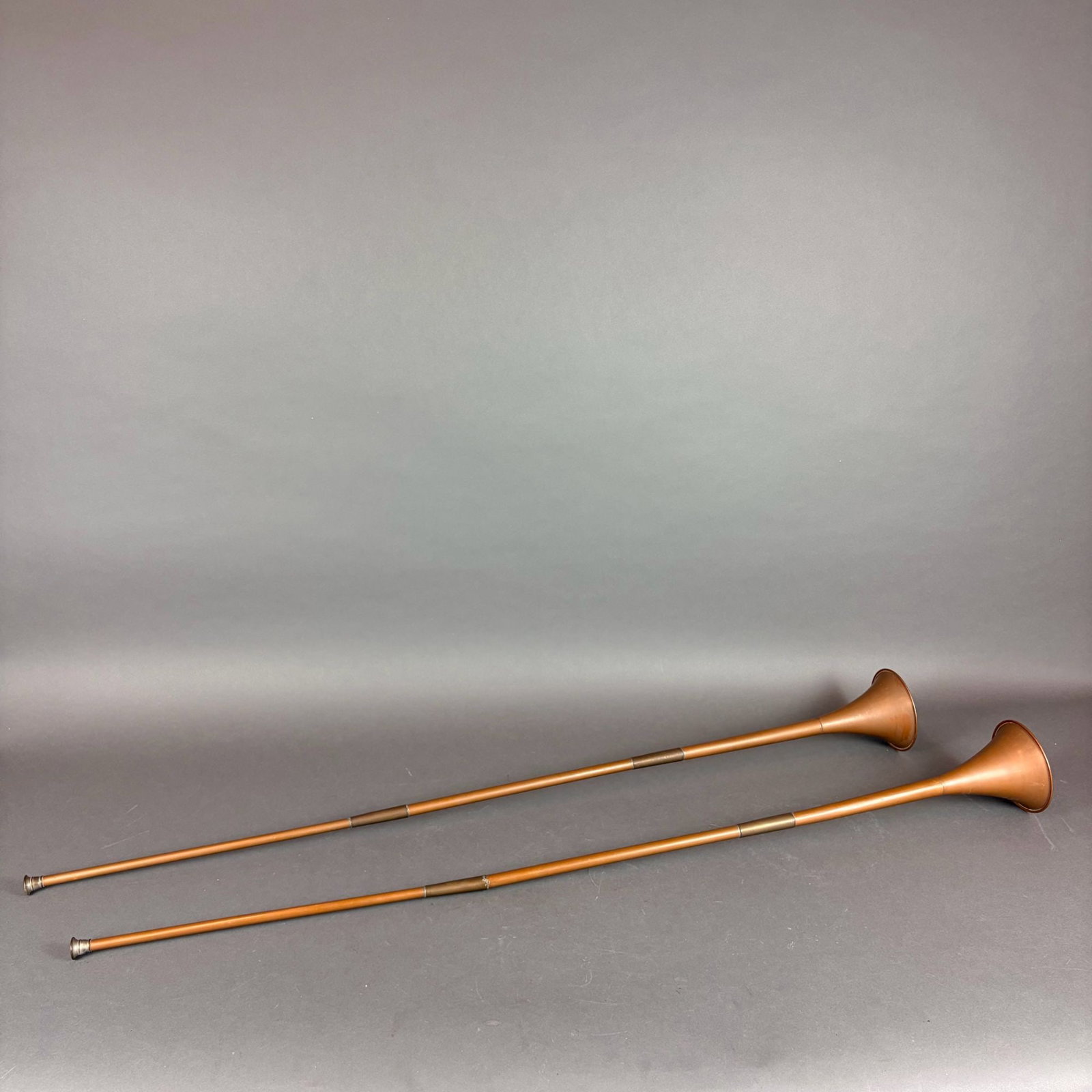 2pc Antique Brass Bugles: Circa 18th/19th century brass bugles features a long, straight form designed for signaling. Each instrument is tapered with visible longitudinal seams and is reinforced with two metal ferrules along t