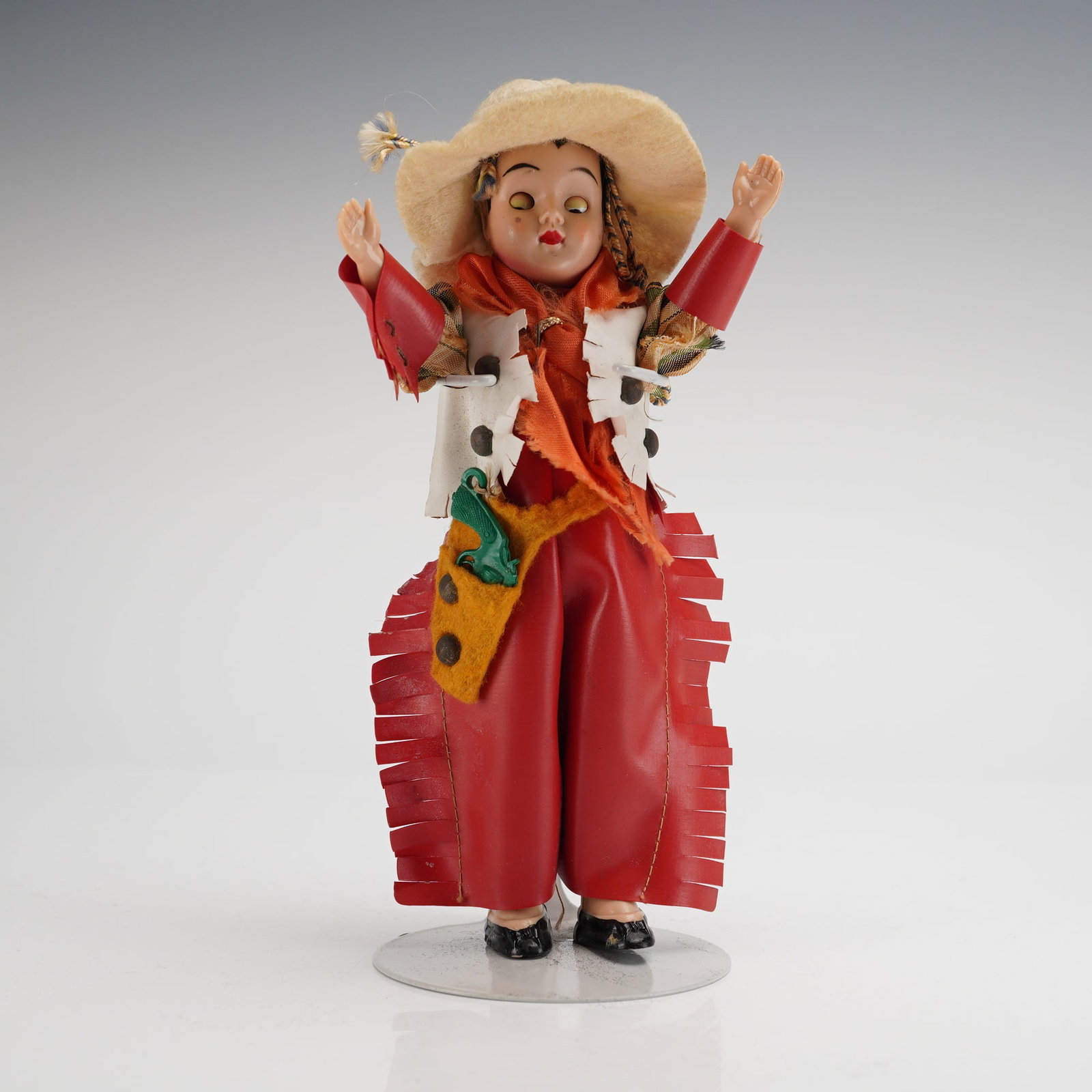 Vintage Western Cowgirl Doll: The figure features a composition or plastic head with movable eyes, painted red lips, and dark hair braided beneath a wide-brimmed cream felt or straw sombrero. The doll is dressed in a regional