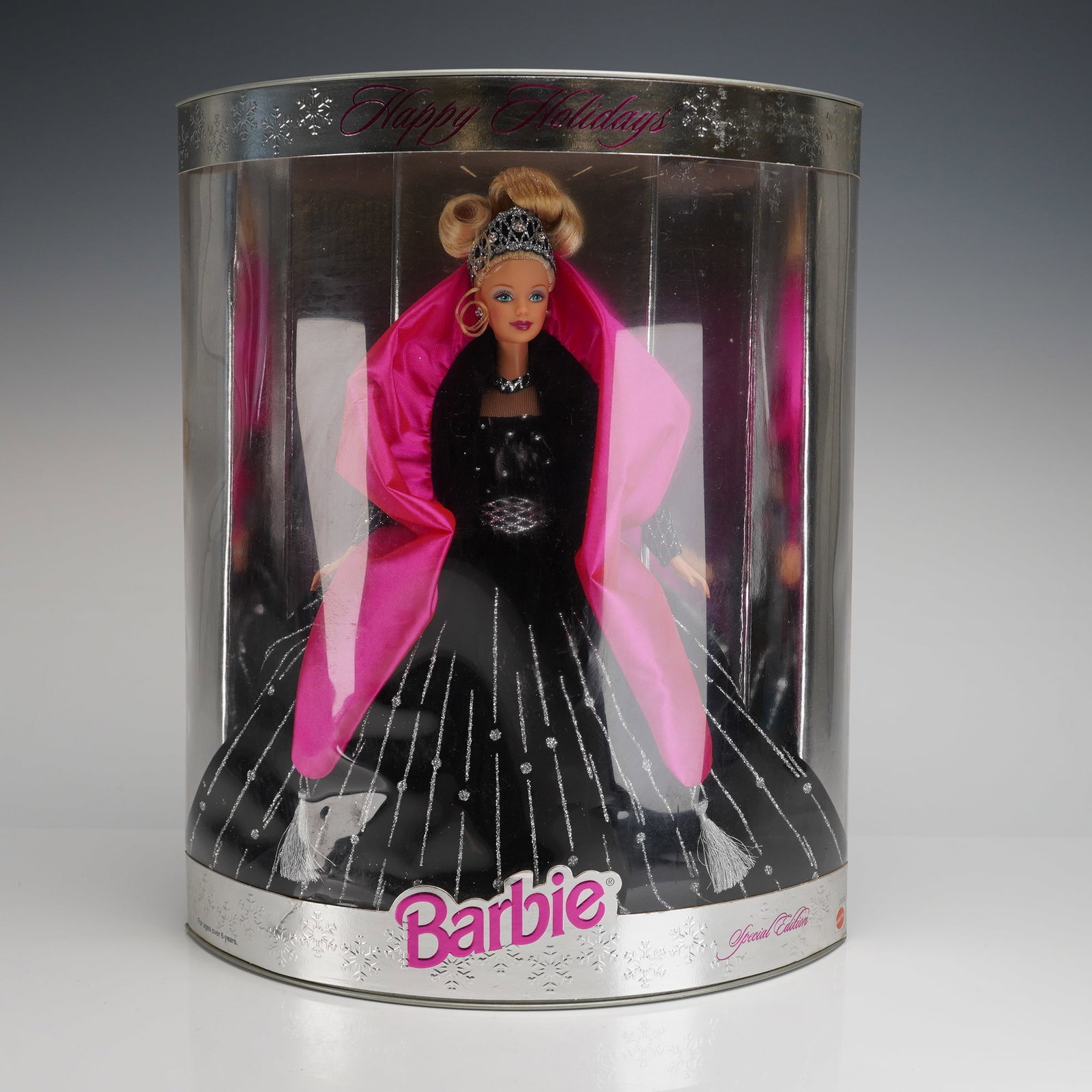 Mattel Happy Holidays Special Edition 1998 Barbie Doll: The doll is presented sealed in its original semi-cylindrical packaging constructed of clear plastic and silver-toned cardboard. The doll wears a black floor-length gown detailed with silver glitter a