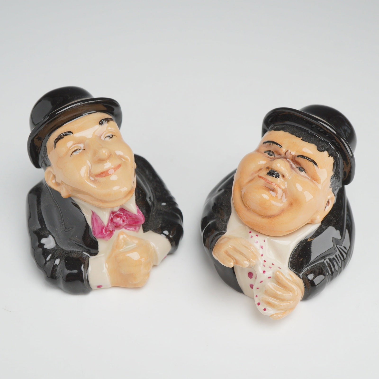 2pc Kevin Francis Face Pots, Stan and Ollie: A pair of polychrome glazed ceramic lidded jars, known as Face Pots, manufactured by Kevin Francis and depicting the comedy duo Laurel and Hardy. The two pieces are modeled from the chest up in a cari