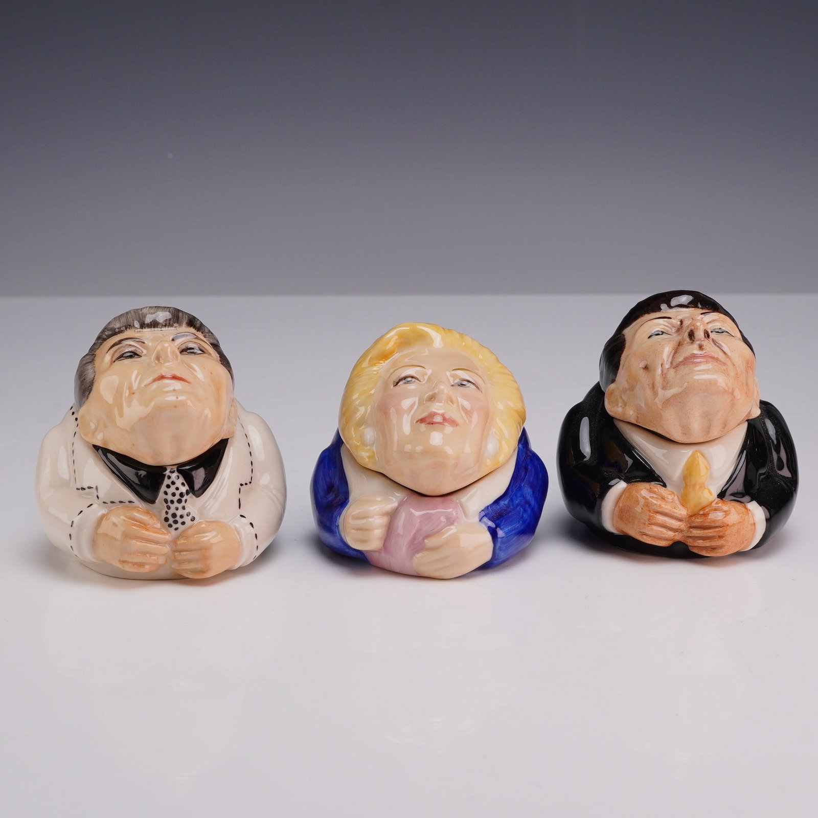 Three Kevin Francis Face Pots, Margaret Thatcher and Ronald Reagan: A trio of glazed ceramic lidded miniature boxes, known as Face Pots, manufactured by Kevin Francis in 2001. Each piece features a caricature portrait lid and a base decorated with attire corresponding