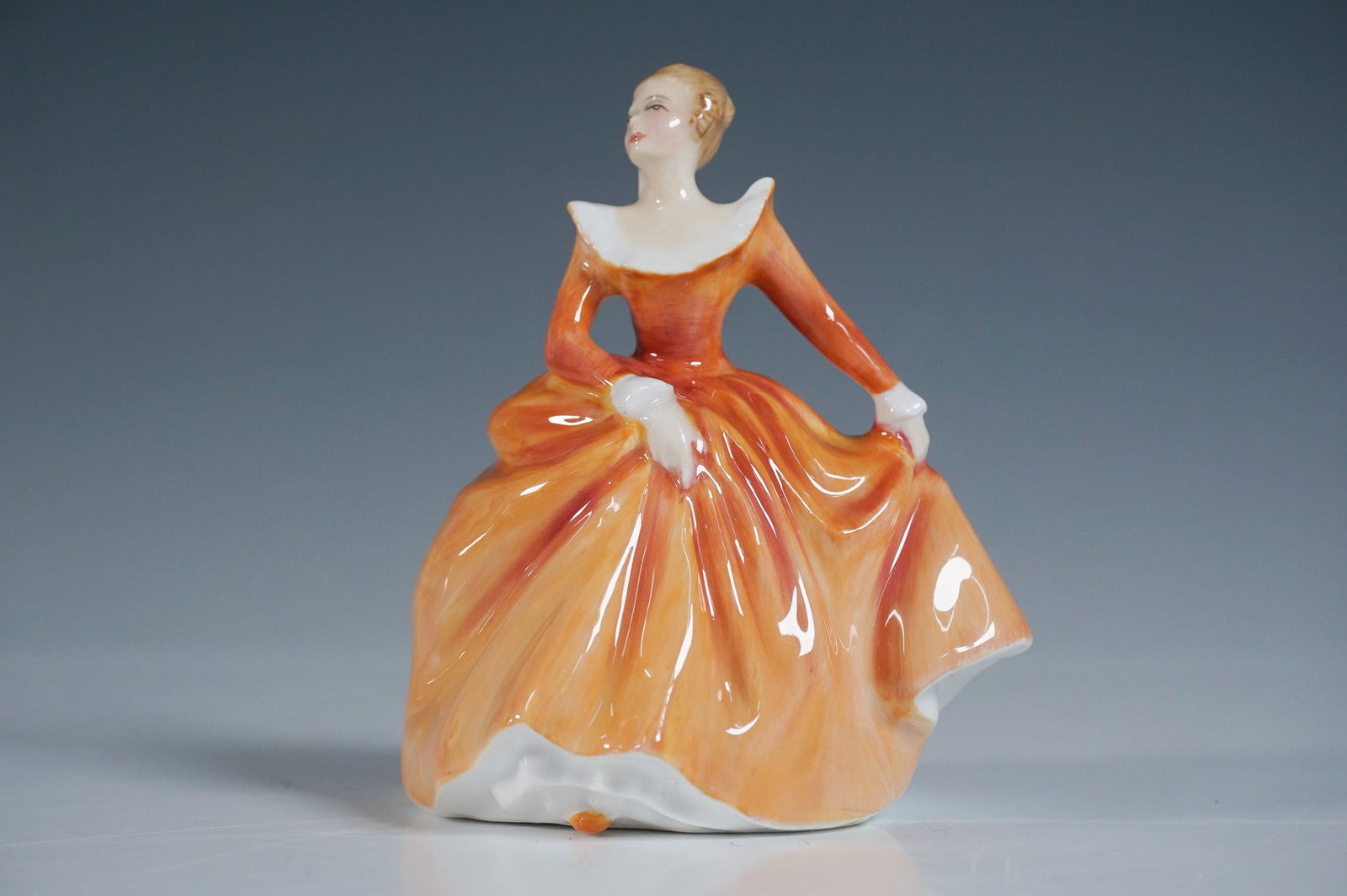 Royal Doulton Fragrance Figurine HN3220: This elegant Royal Doulton bone china figurine, titled Fragrance (HN 3220), was designed by renowned artist Peggy Davies in 1965. The figurine features a graceful lady in a flowing orange gown, captur