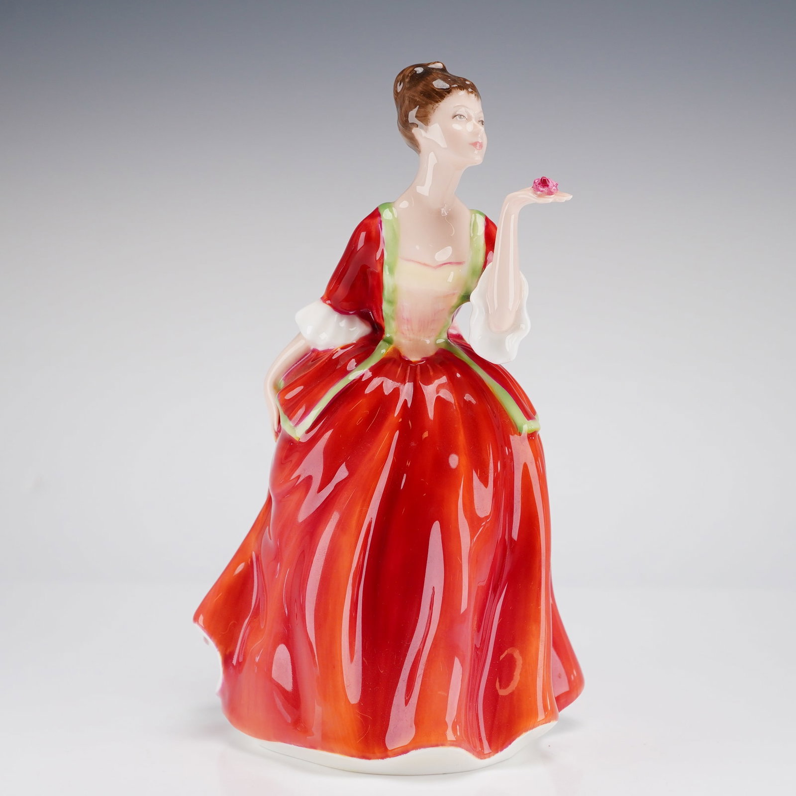 Royal Doulton Figurine Flower of Love HN3970: A glazed bone china figurine by Royal Doulton, depicting a woman in a flowing red, white, and cream dress, holding a pink rose. The underside features the Royal Doulton backstamp, the title, model num