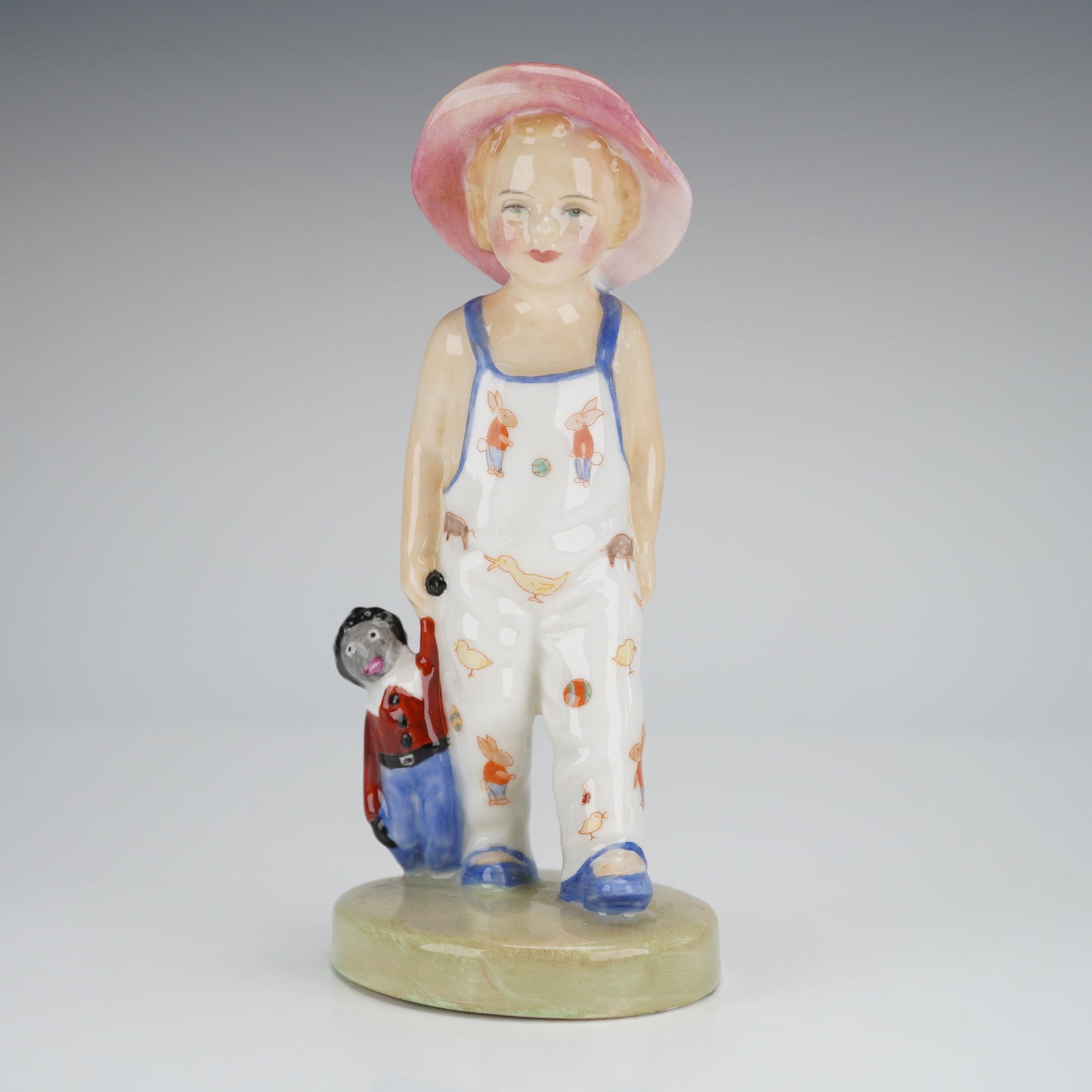 Royal Doulton Figurine Golliwog HN1979: A Royal Doulton bone china figurine, model number HN1979, titled "Golliwog." The figurine depicts a child wearing white overalls decorated with polychrome animal and bird motifs, and a wide pink sun h