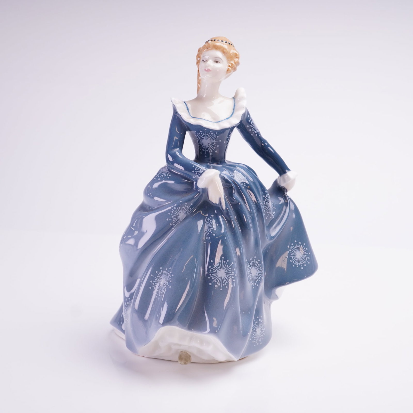 Royal Doulton Fragrance HN2334 Bone China Figurine: This Royal Doulton bone china figurine, titled Fragrance HN2334, depicts a woman in a full-skirted blue gown decorated with white starburst patterns. The figure features a white ruffled collar and cuf