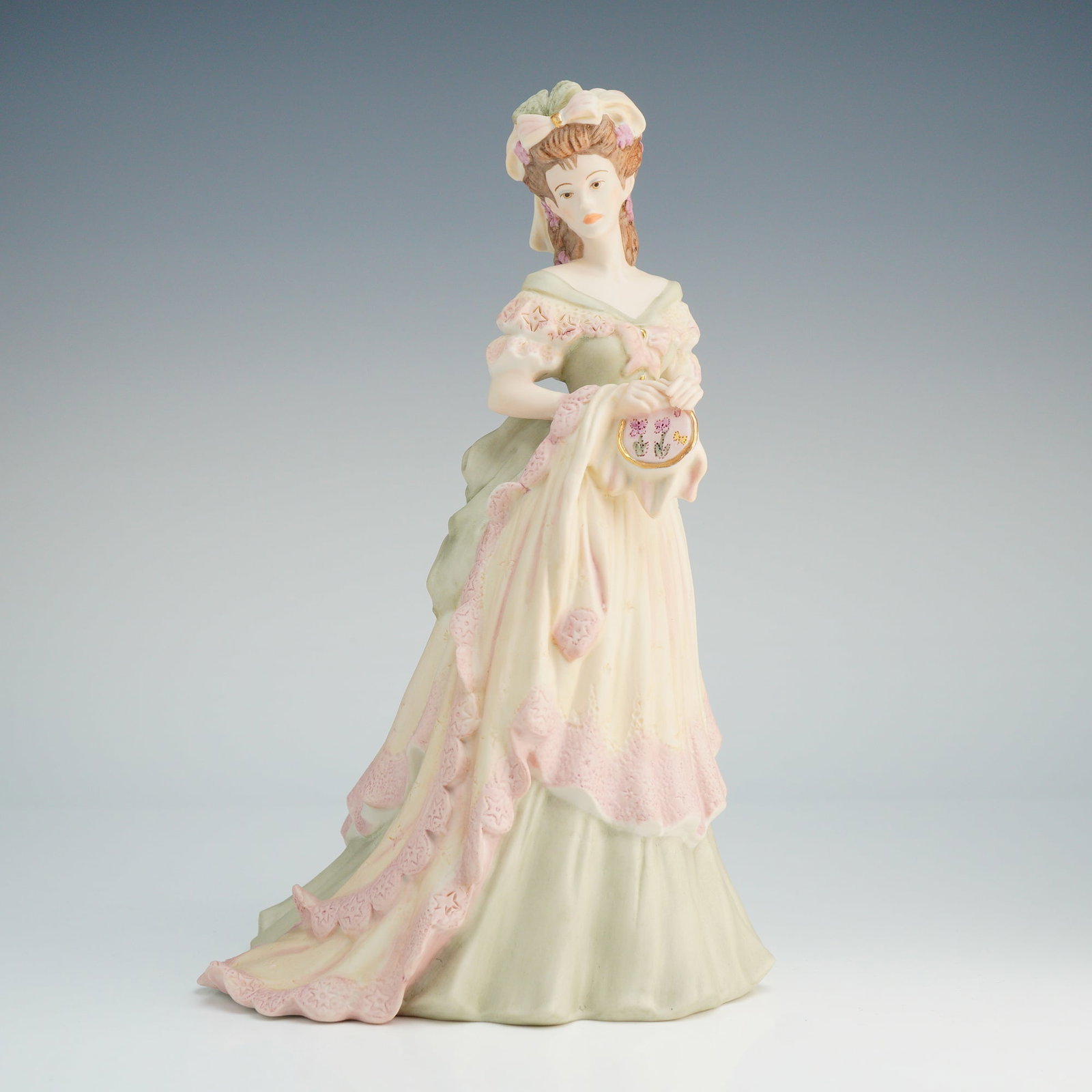 Coalport Porcelain Figurine, Age of Elegance Tapestry: A Coalport matte bisque porcelain figure is modeled in late 18th-century style dress, featuring a tiered gown in pale green and cream tones with pink lace-patterned borders. The subject is depicted ho
