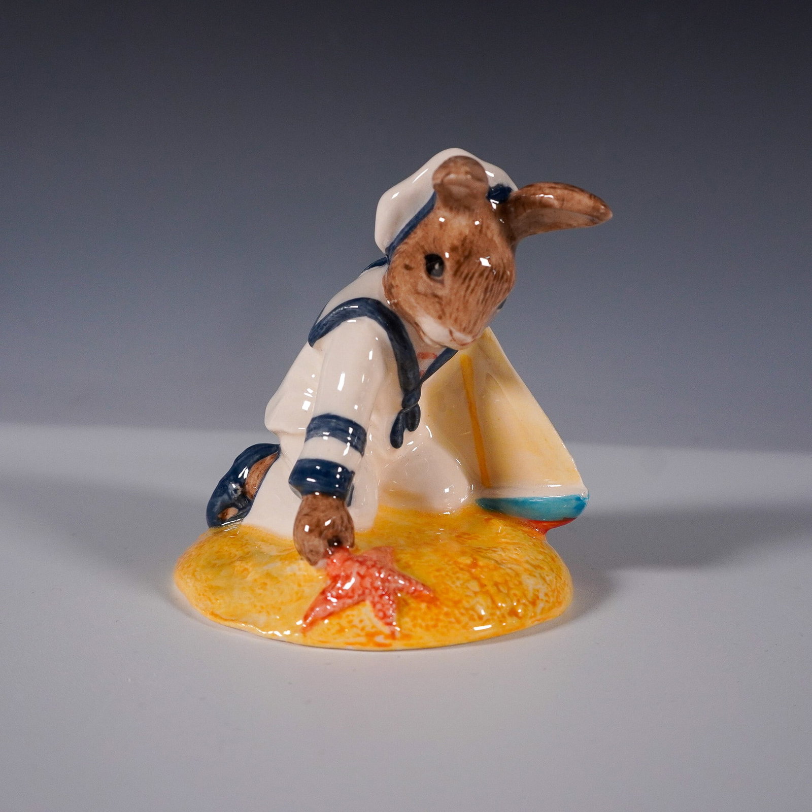 Royal Doulton Bunnykins Figurine, Sailor Bunnykins D166: Royal Doulton Bunnykins figurine titled "Sailor Bunnykins" (D166), designed in 1987. This delightful figurine features a sailor bunny in a white and blue uniform holding a sailboat and reaching for a 