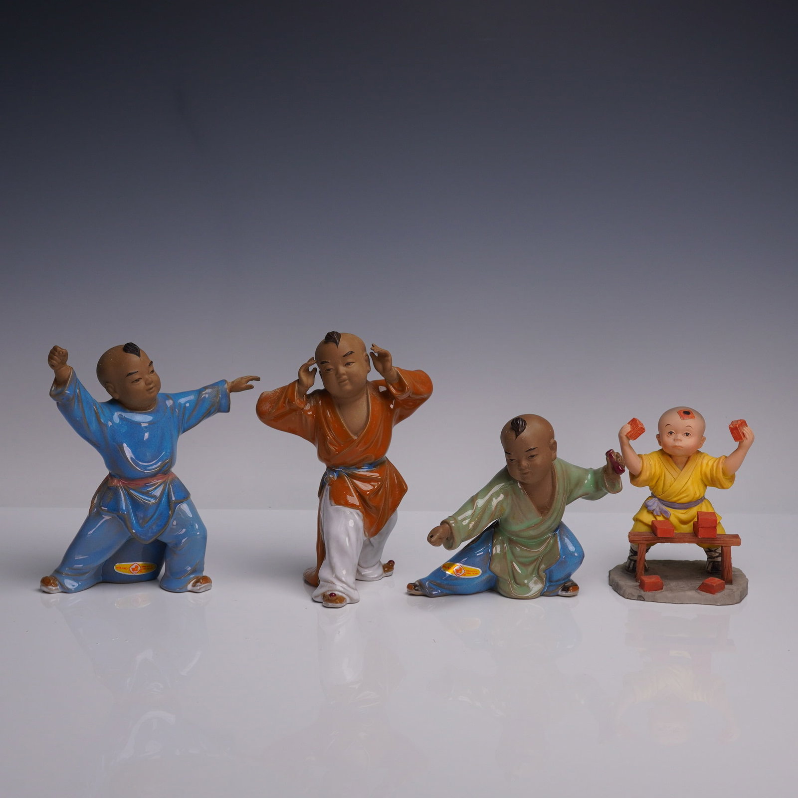 4pc Chinese Porcelain Children Figurines: A lively 4-piece group of Chinese porcelain figurines depicting young boys in dynamic poses. Each figure is hand-painted in bright robes of blue, orange, green, and yellow, with expressive facial feat