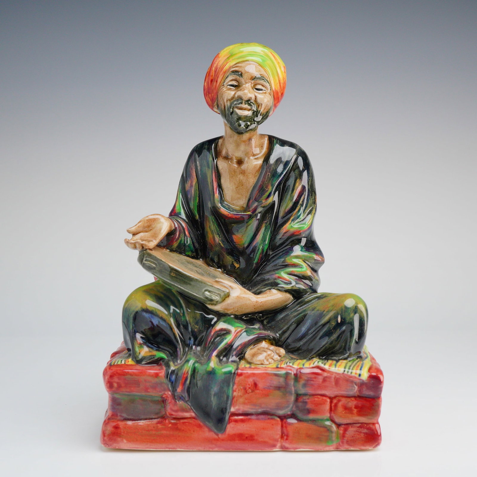 Royal Doulton Porcelain Figurine, Mendicant HN1365: A Royal Doulton glazed porcelain figurine titled The Mendicant, identification number HN 1365. The figure depicts a man with a black beard and a yellow and orange turban, seated cross-legged on a red 