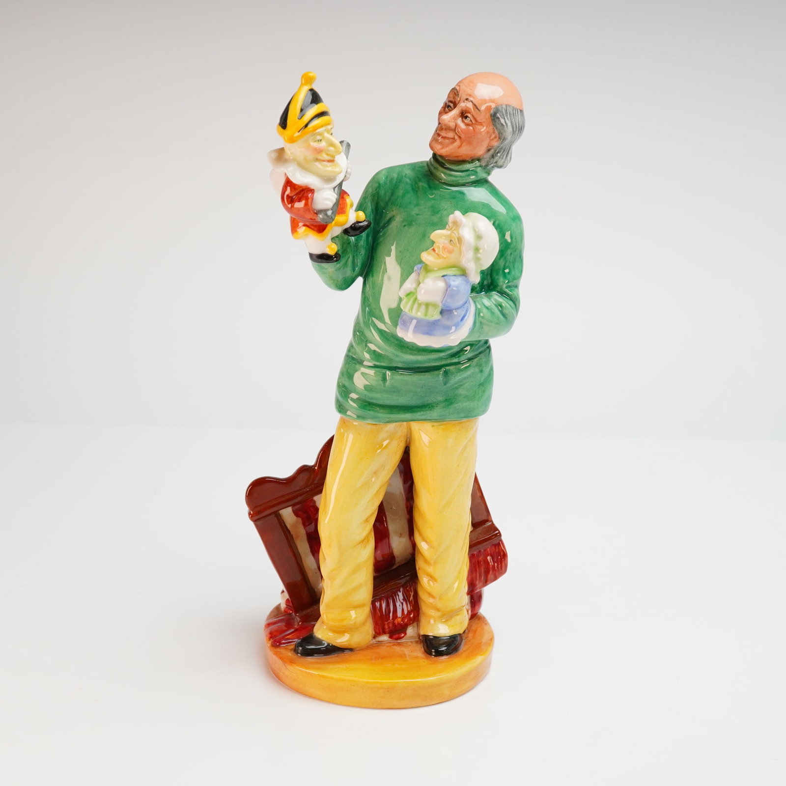 Royal Doulton Porcelain Figurine, Punch & Judy Man (HN2765): A Royal Doulton glazed porcelain figurine titled Punch and Judy Man, model number HN 2765. The piece depicts a standing man with a partially bald head wearing a green turtleneck sweater and yellow tro