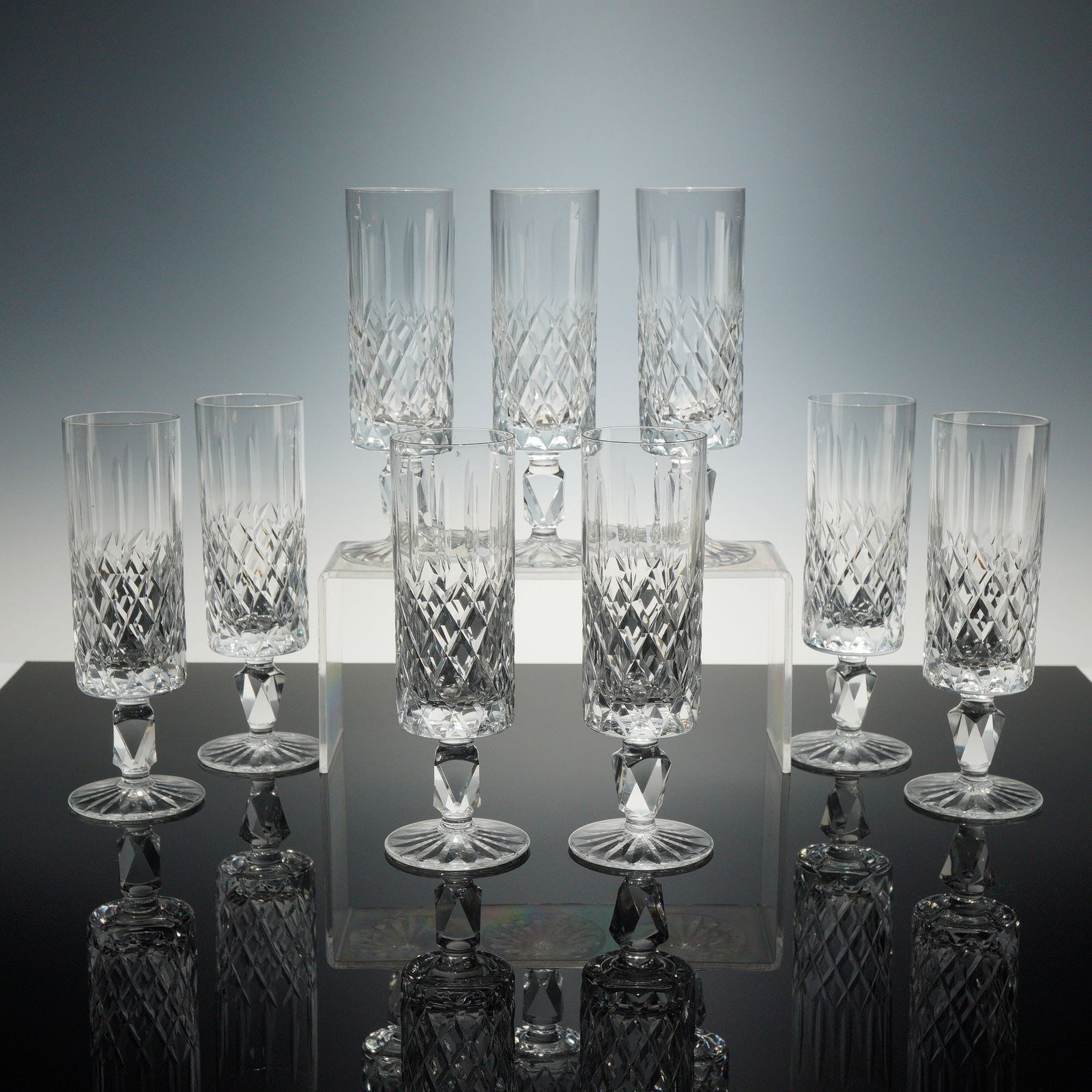 Set of Nine Waterford Crystal Champagne Flutes, Lismore Simplicity: A set of nine champagne flutes crafted from lead crystal in the Lismore pattern by Waterford. The design consists of a cylindrical bowl with deep diamond criss-cross cuts on the lower portion and vert
