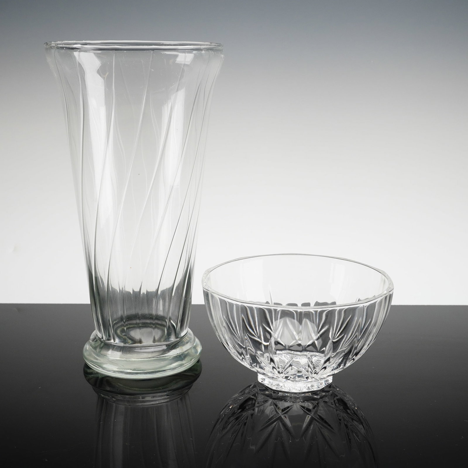 2pc Clear Cut Glass Bowl and Vase: This duo includes one cut glass bowl and one vase. The group includes a tall trumpet-form vase featuring a subtle optic spiral design within the body, supported by a substantial, thick circular base. 