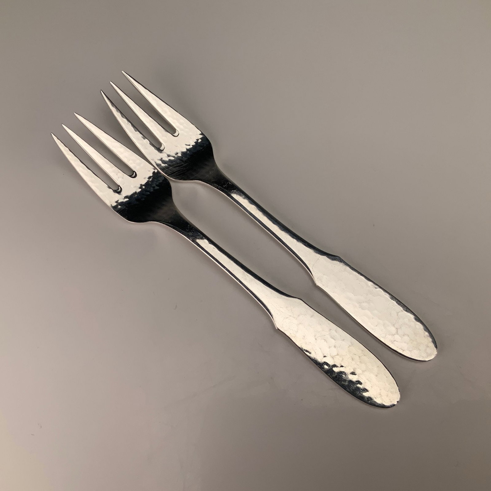 A Pair of Georg Jensen Denmark EPNS Mermaid Pattern Hammered Fish Forks: This pair of fish forks is manufactured by Georg Jensen of Denmark in the Mermaid pattern. The items are constructed from electroplated nickel silver, as indicated by the EPNS designation. The design 