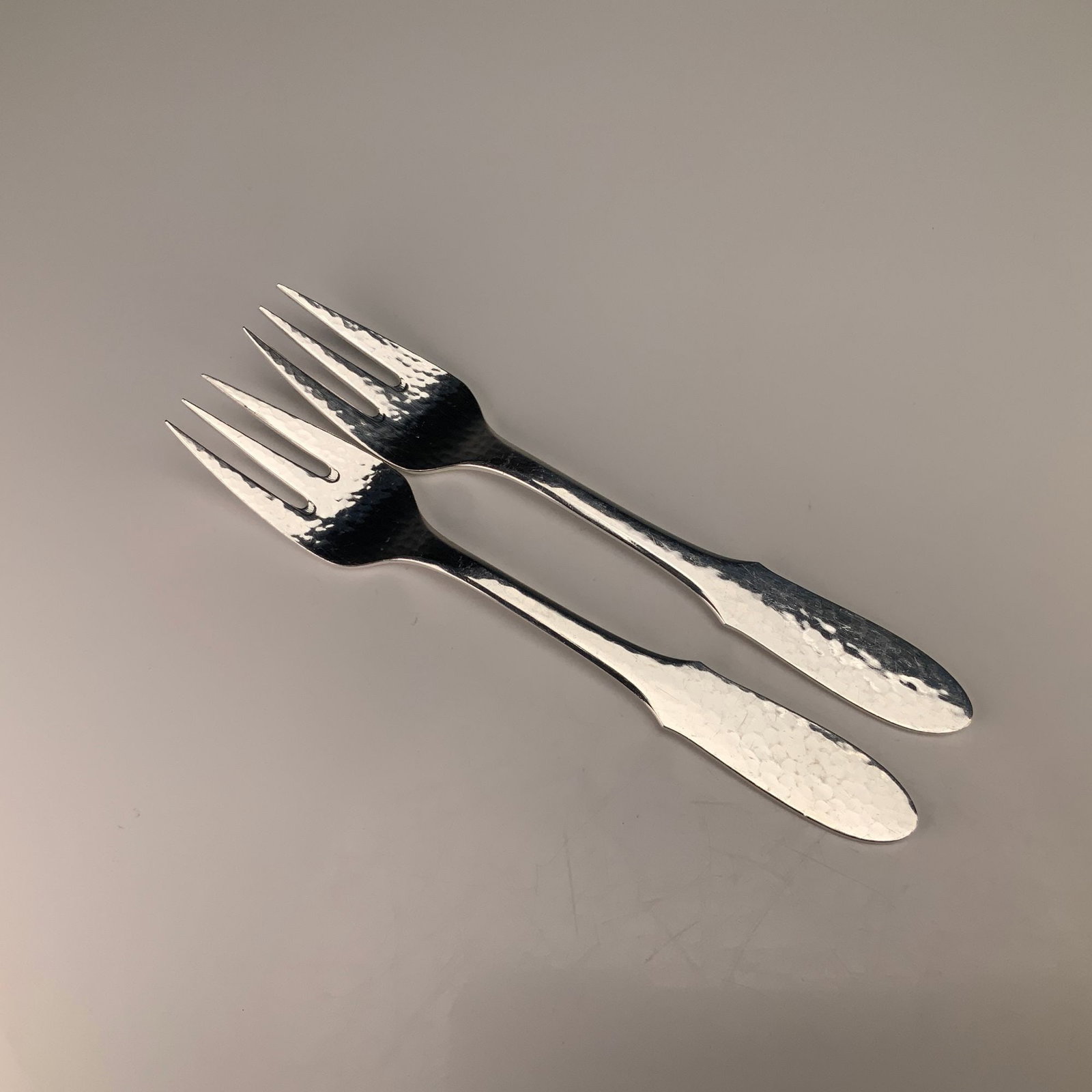 A Pair of Georg Jensen Denmark EPNS Mermaid Pattern Hammered Fish Forks: This pair of fish forks is manufactured by Georg Jensen of Denmark in the Mermaid pattern. The items are constructed from electroplated nickel silver, as indicated by the EPNS designation. The design 