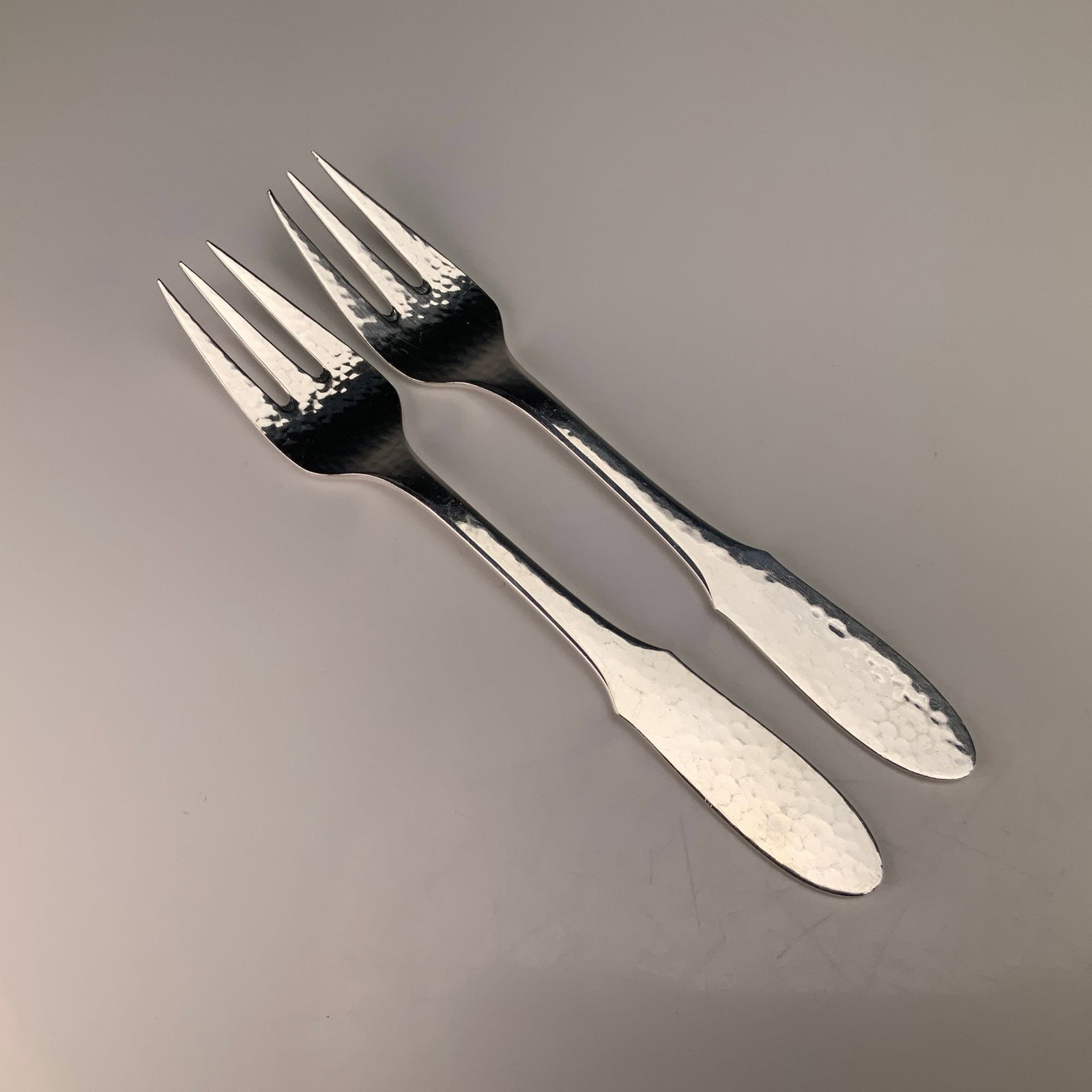 A Pair of Georg Jensen Denmark EPNS Mermaid Pattern Hammered Fish Forks: This pair of fish forks is manufactured by Georg Jensen of Denmark in the Mermaid pattern. The items are constructed from electroplated nickel silver, as indicated by the EPNS designation. The design 