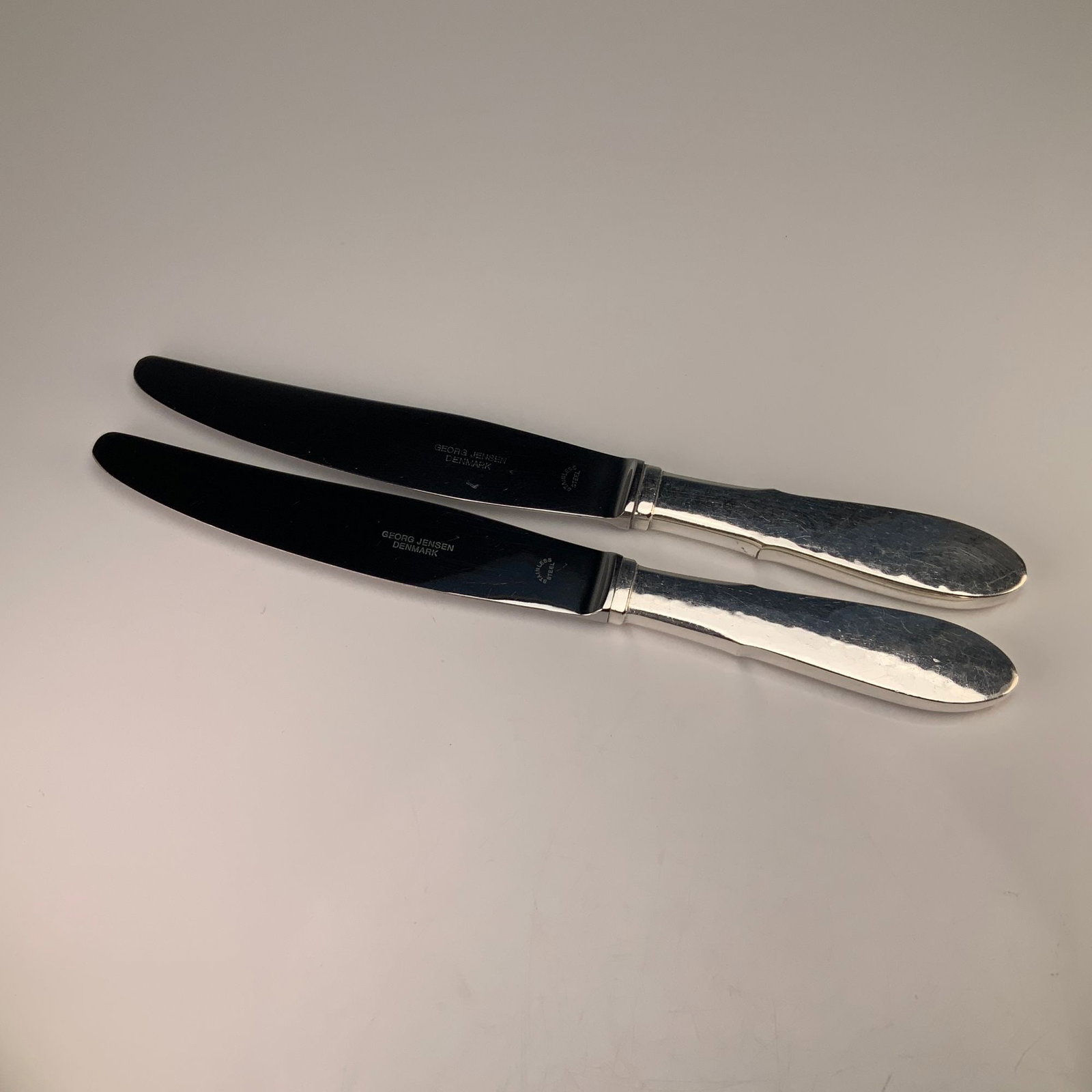 A Pair of Georg Jensen Denmark Mermaid Pattern EPNS Knives: This pair of dinner knives is produced by Georg Jensen of Denmark in the Mermaid pattern. The handles are constructed of electro-plated nickel silver (EPNS) and feature a hand-hammered texture with a 